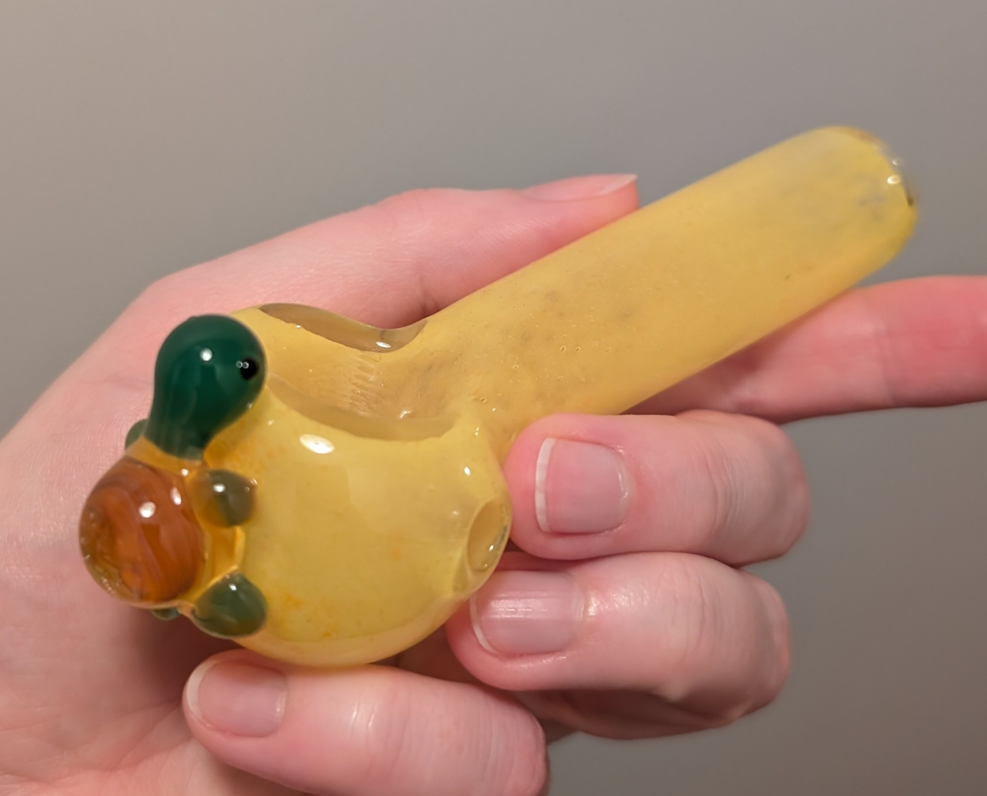 a yellow blown glass weed pipe with a cute little green turtle with a brown shell on the back edge of the bowl