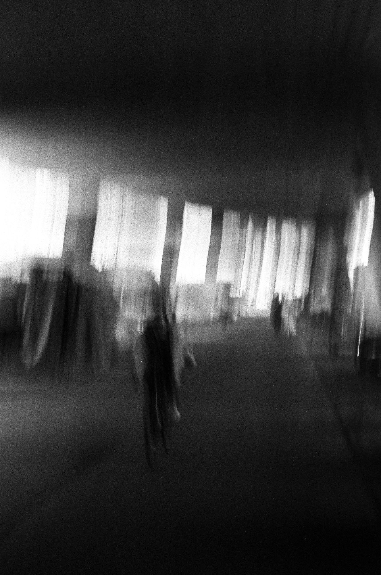 Submerged in shrouds of a dying star we window shop the spectacle

a blurry black and white photo of an underground place or under a bridge, a person riding a bicycle towards the viewer, a couple of persons in the far back in robes or dresses. Light leaks into the room as a haze from the left