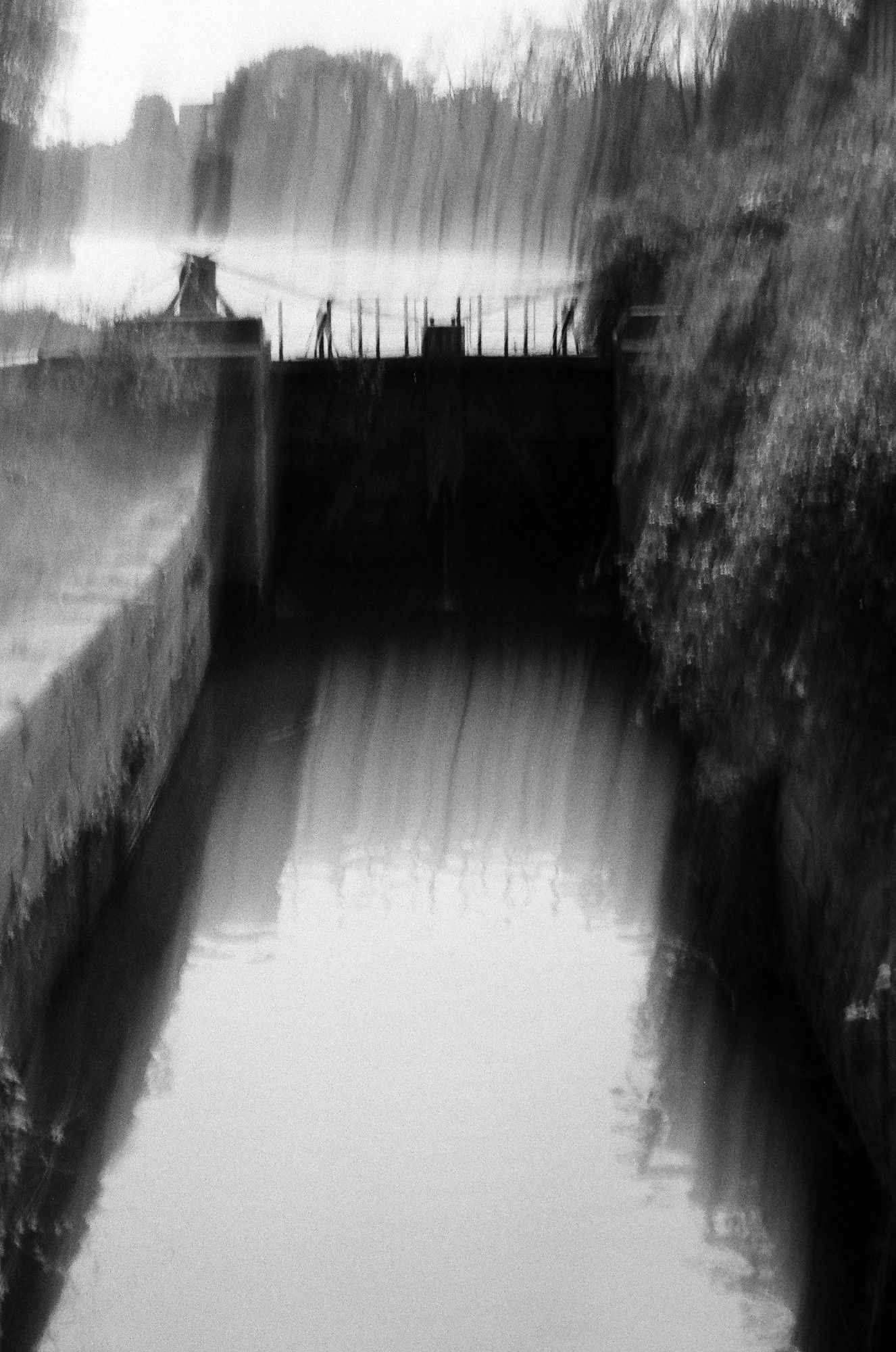 as the gate leaks souls into creation's stream it aches under the pressure of the boiling melange of old an new spirits

a black and white blurry, hazy photo of a small gate holding back a seemingly evaporating river while a small stream is in front of the viewer