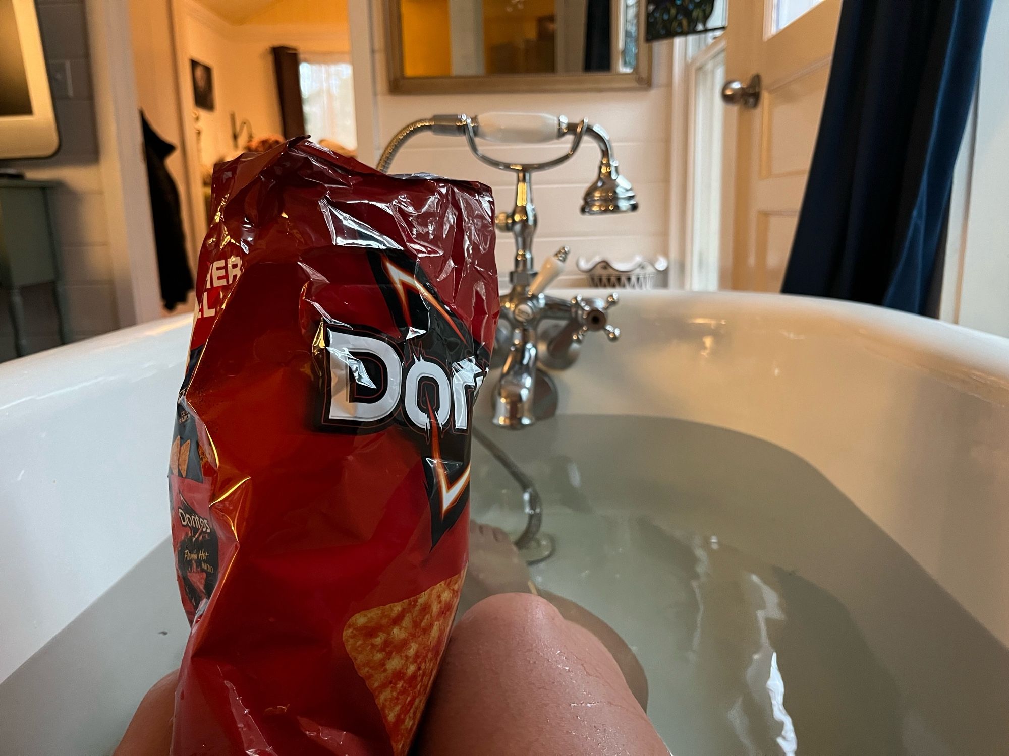 D enjoying a full sized bag of nacho cheese Doritos in a bathtub.