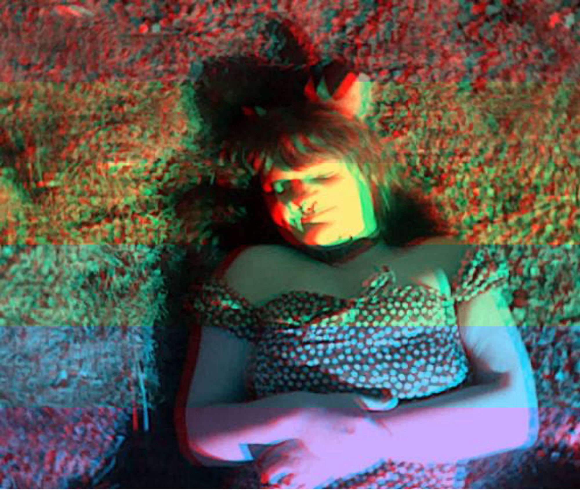 A picture taken on a 3ds of a trans woman in a polka dot dress laying in the grass in dog ears with a rainbow stereoscopic filter