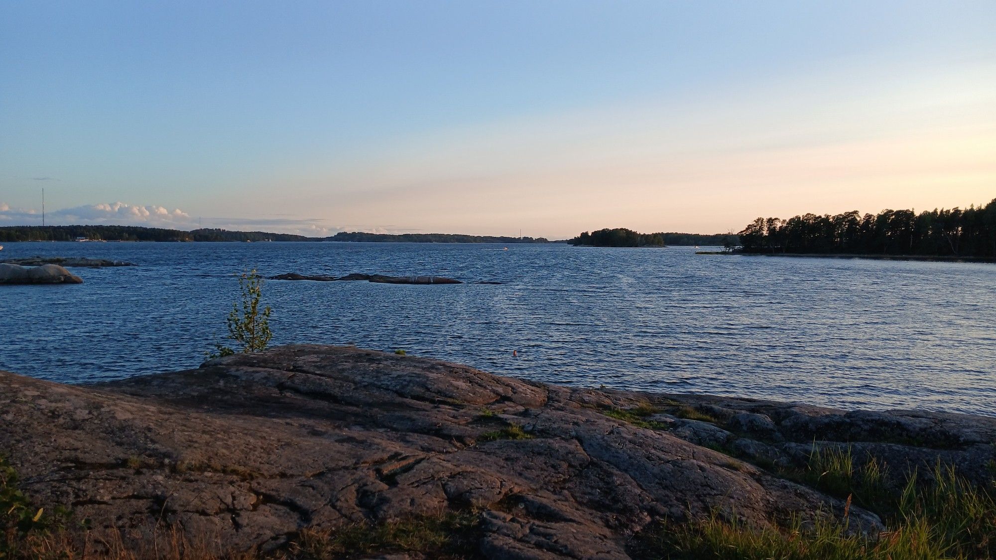 Kumpukerrospilviä kaukana Santahaminan (takana vasemmalla) yllä, Hevossalmen Vuorilahden uimarannan viereiseltä kalliolta hieman ennen auringonlaskua kuvattuna. Etuvasemmalla lähempänä luonnonsuojelualueen kallioluotoja. Etuoikealla taaempana Koivusaari ja lähempänä Stansvikin Tahvonlahdenniemen luonnonsuojelualueen niemenkärki. Kuvanottopaikan kallioalueelta on louhittu 1940-luvulla hetken aikaa granaattia (mineraali), josta tehtyjä lattialaattoja löytyy ainakin Ruoholahden kaapelitehtaan lattiasta. Laajasalo, Helsinki.