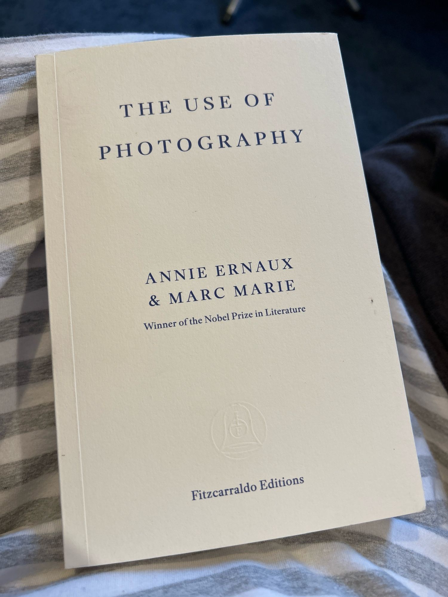 Photograph of a copy of “The Use of Photography” by Annie Ernaux and Marc Marie, published by Fitzcarraldo Editions. A small plain cream cover with navy blue lettering.