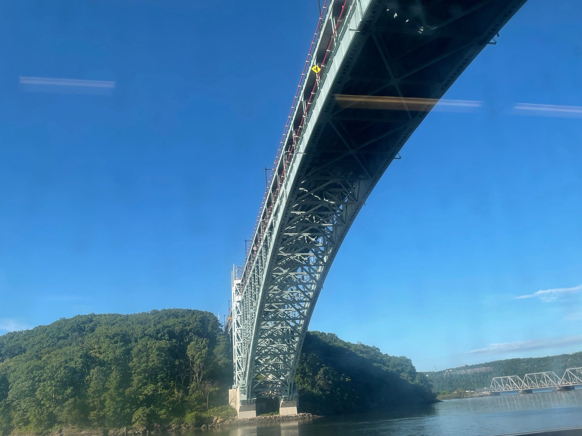 Henry Hudson Bridge, viewed from below (from MetroNorth train on tracks at Spuyten Duyvil) with Inwood Hill, Hudson River and NJ palisades in background on a beautiful sunny morning with blue sky