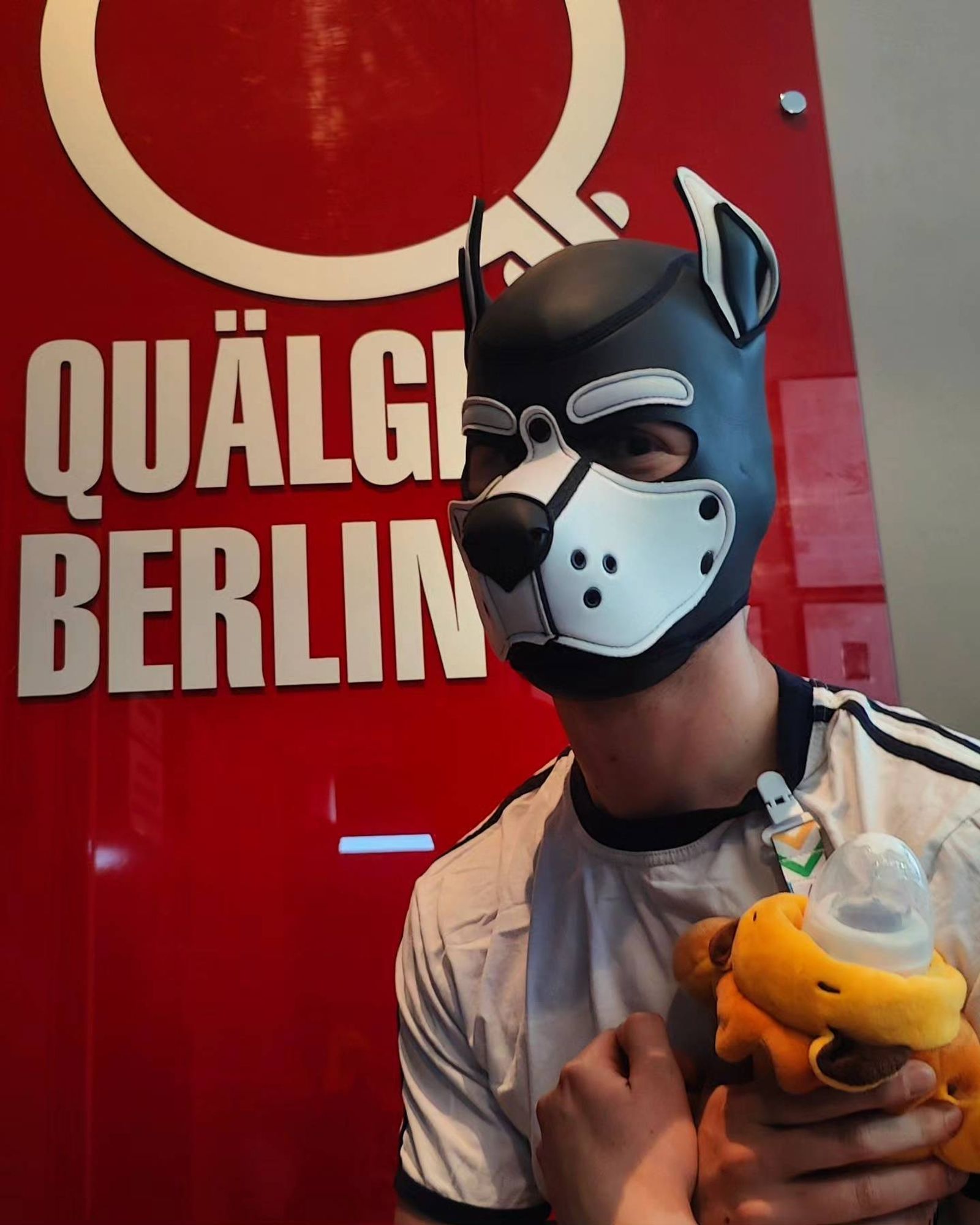 Robin wearing his puppy mask and holding his bottle, posing in front of the Quälgeist sign.