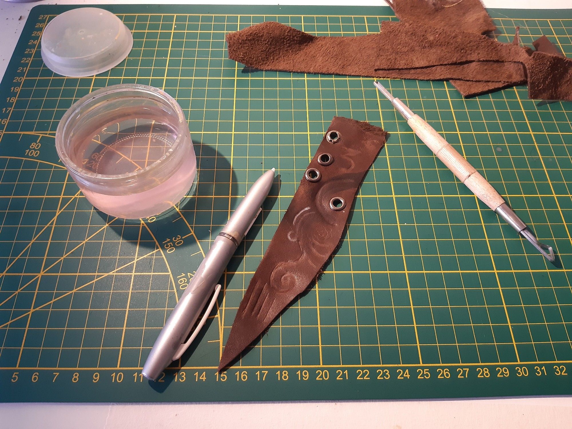 Pieces of leather on a cutting mat.
There's a graphic tablet's pen beside it.

The leather is covered with random lines as I was learning how to carve in it. There are also eyelets on one side, as I was learning how to hemmer them properly.