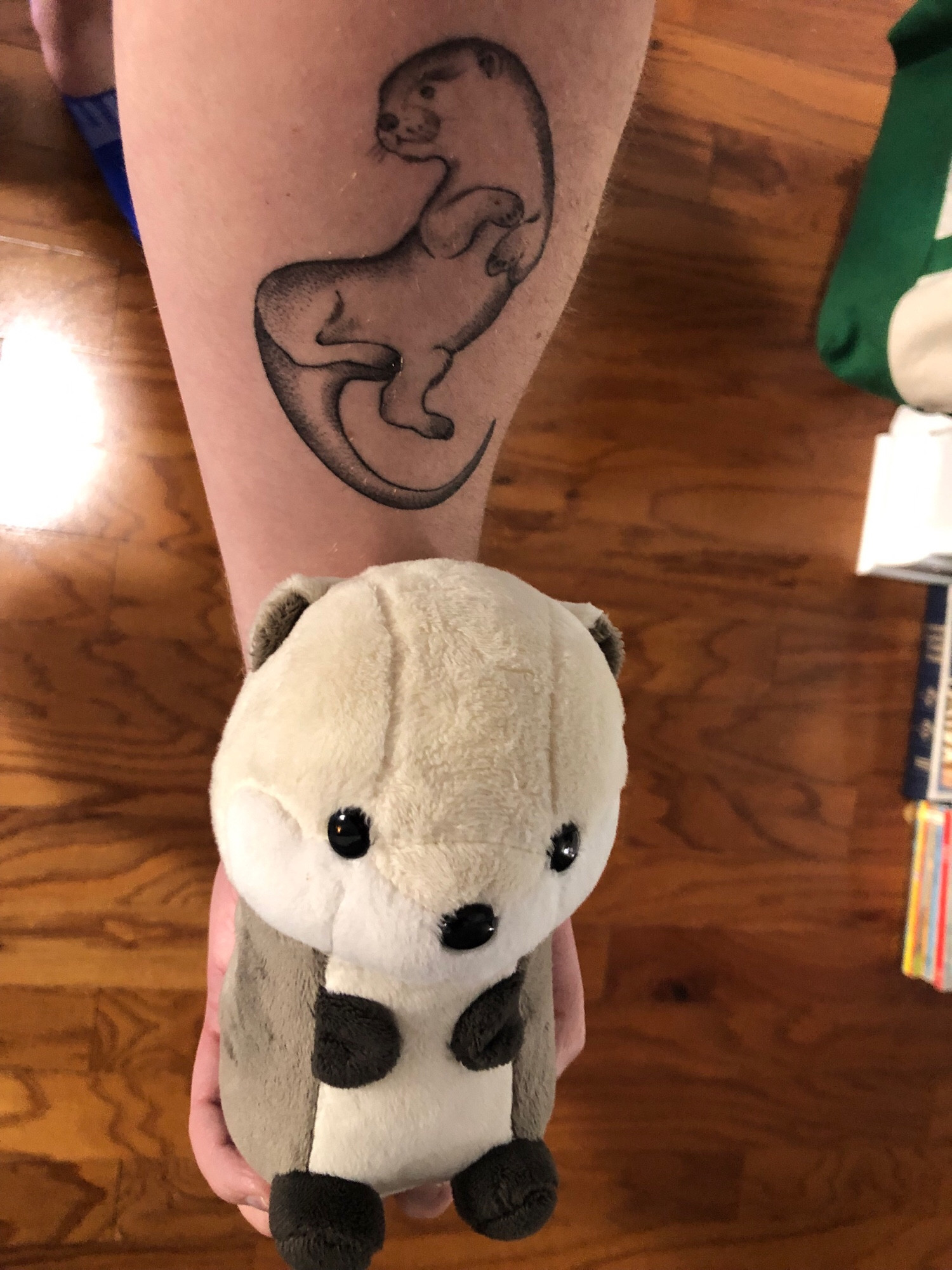 small stuffed otter with beige head and belly and brown sides and paws held by a person with an otter tattoo on their forearm. you can’t see the person’s feet