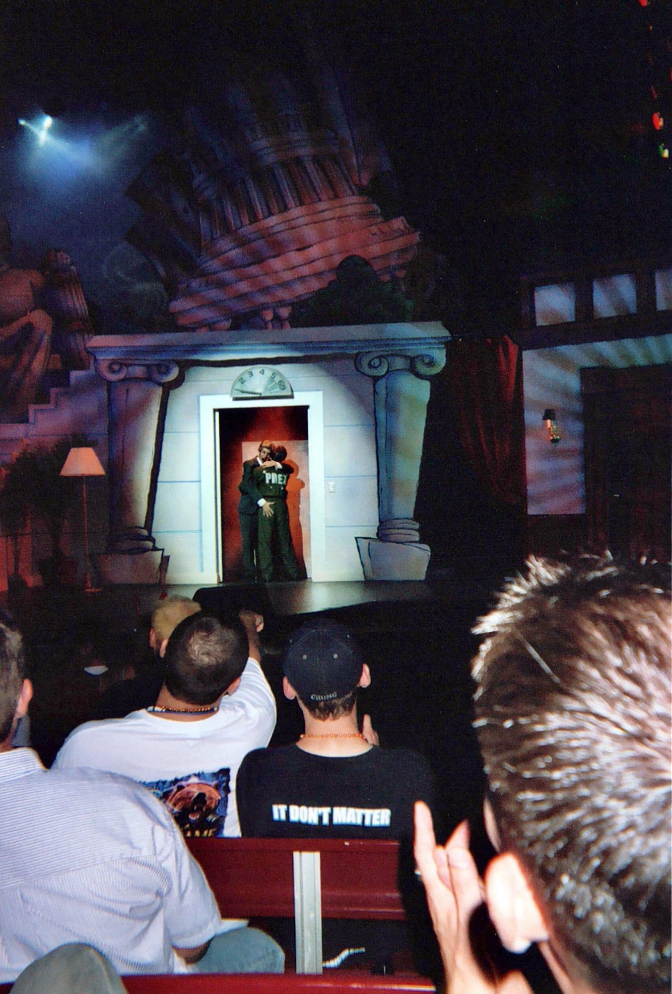 From Bill and Ted 2004. On stage, two men slow dance in the doorway of a stylized government building, their arms wrapped around each other. One has his back to the audience, wearing a black jacket that reads “PREZ” in white letters—George W. Bush. The other, facing the audience, is John Kerry. John Kerry’s right hand hovers just over Bush’s tight ass.