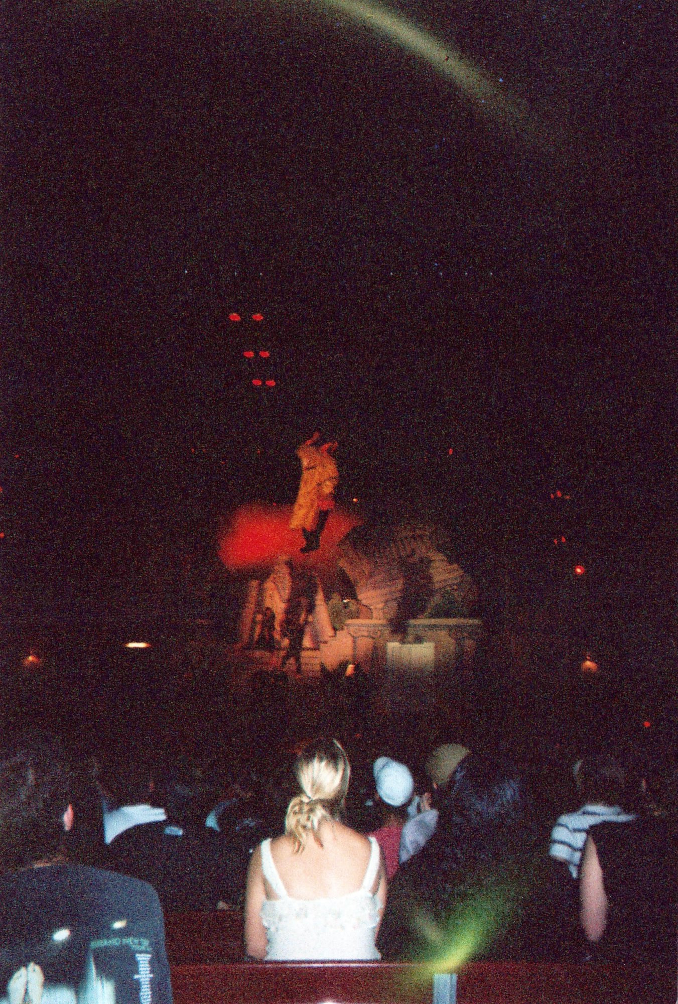 From Bill and Ted, a performer dressed as Hellboy, wearing a brown trench coat, rappels from above the stage. The red spotlighting hides the rest of the stage.