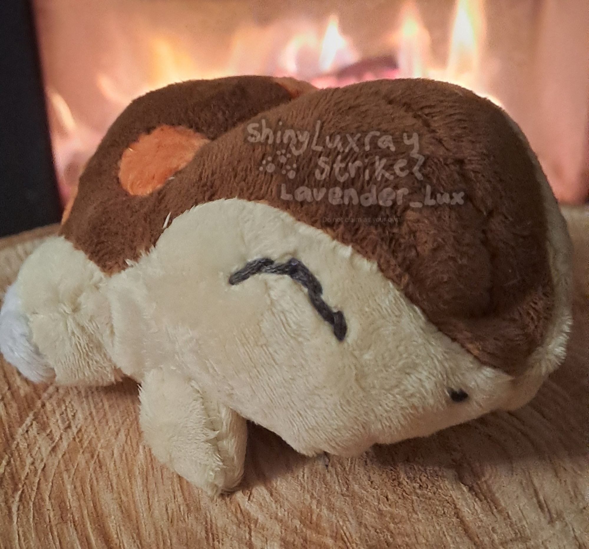 Custom plush of shiny Cyndaquil. Pattern is from a bootleg Cyndaquil pokedoll I seam ripped. 

Cyndaquil, a tan colored pokemon with closed eyes and a brown back with 4 red dots, lies on a piece of wood in front of a fireplace.