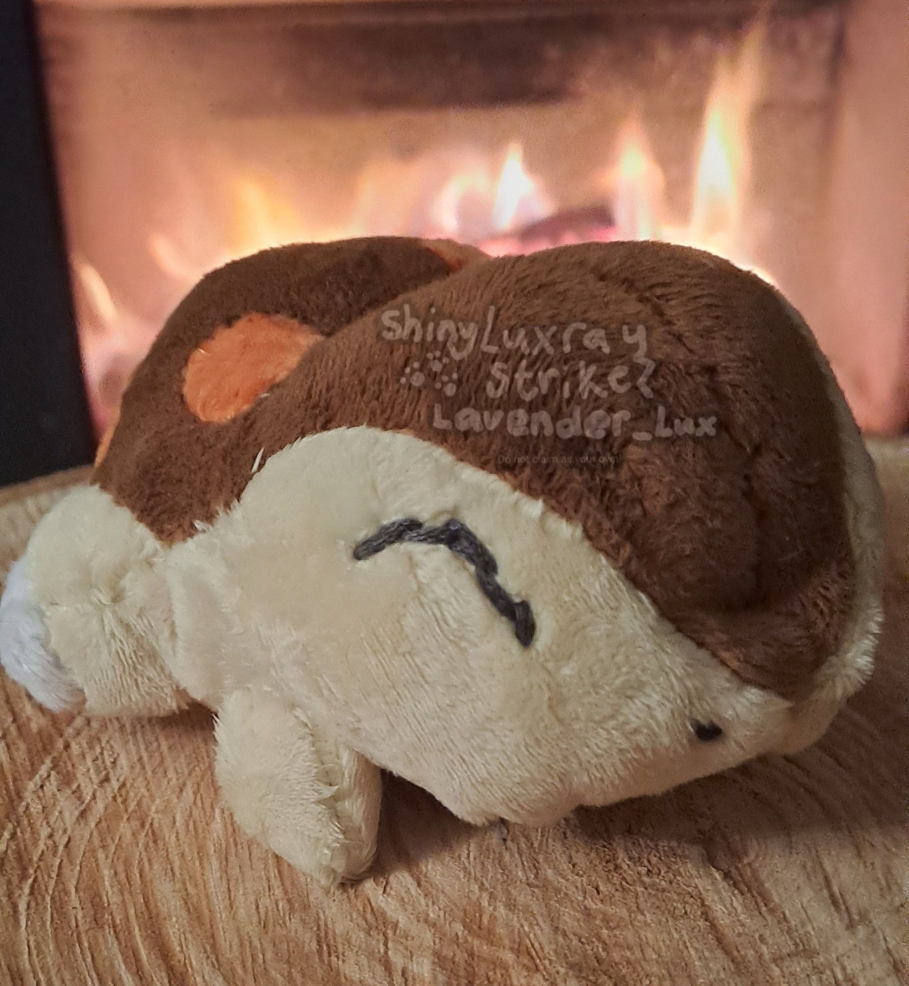 A shiny Cyndaquil pokedoll lying on a log in front of a fireplace