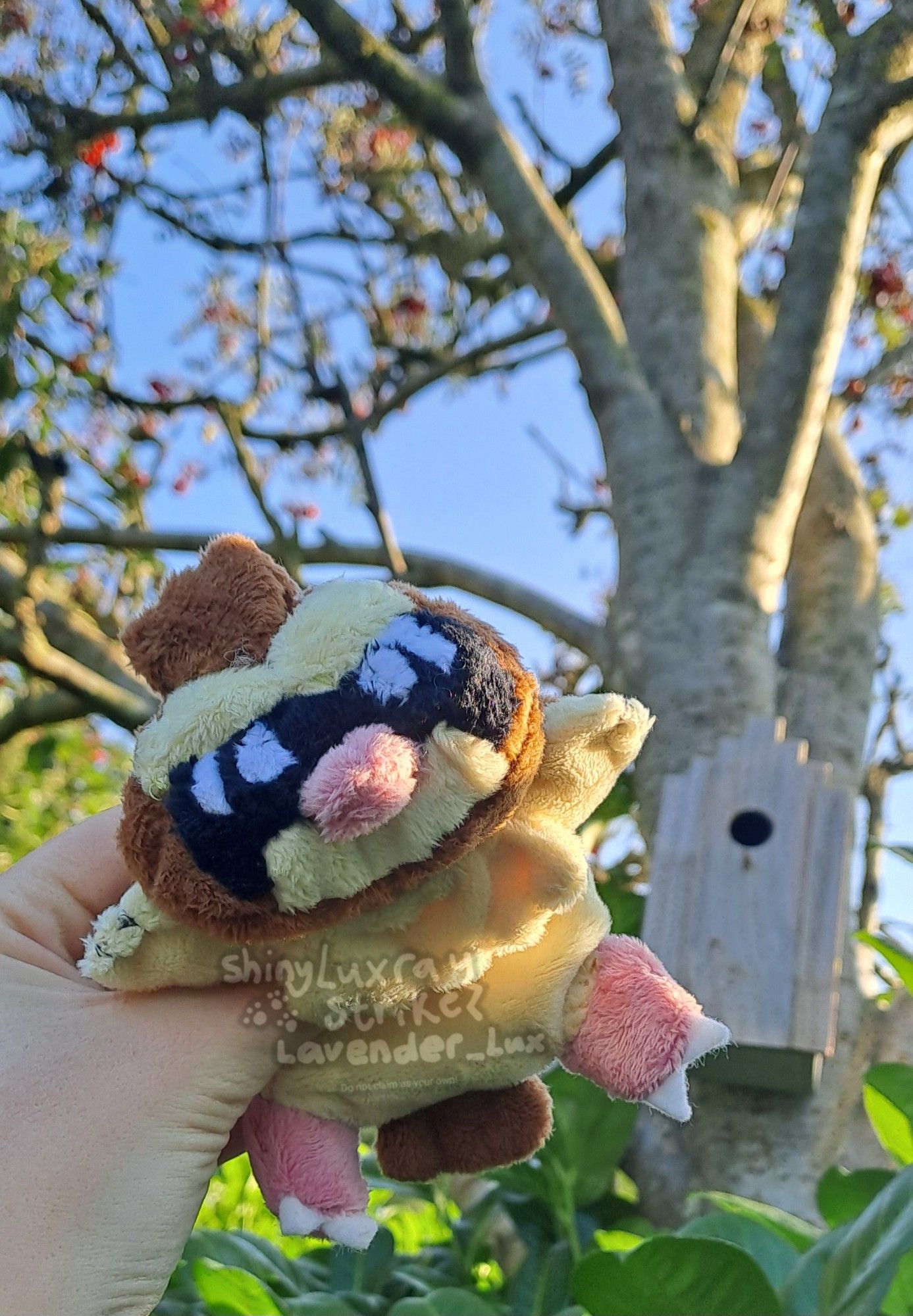 A Pidgey beanie/kuttari plush held up against a blue sky and tree with bird house. Base pattern by syleniscrafts