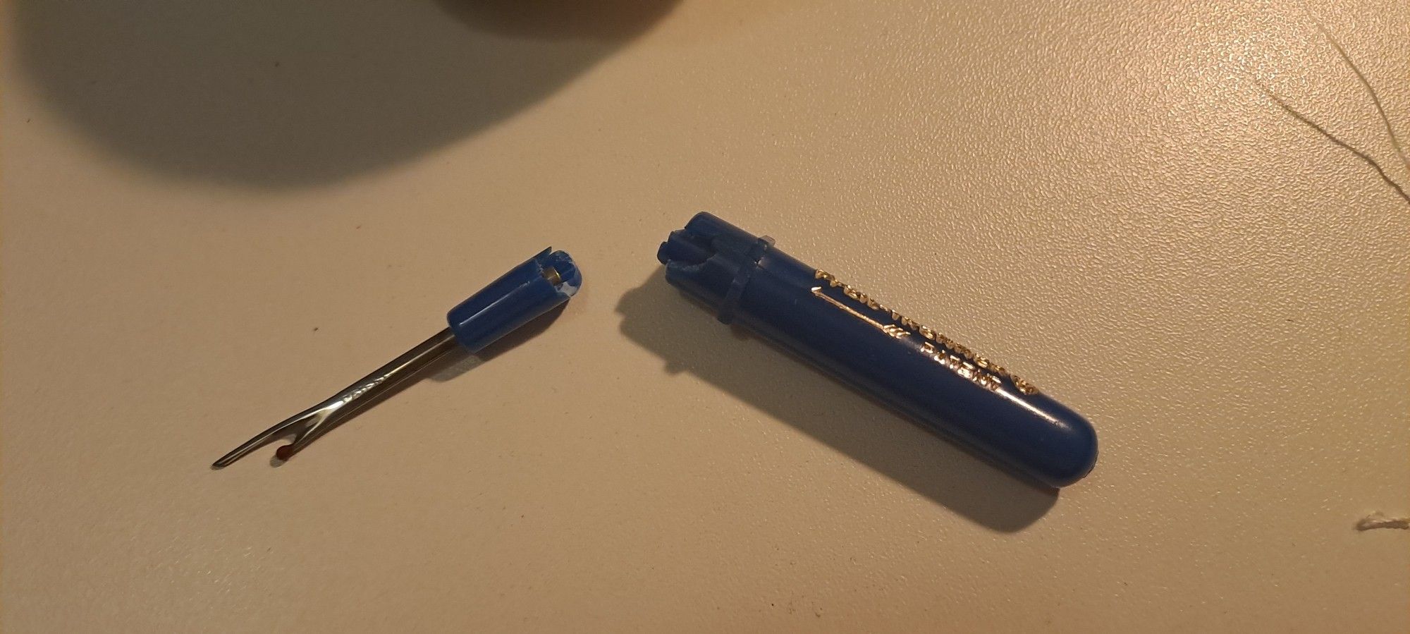 Picture of a white desk, luminated by an off-screen desk lamp. In the middle is a sewing tool, a seam ripper, which is broken in two pieces