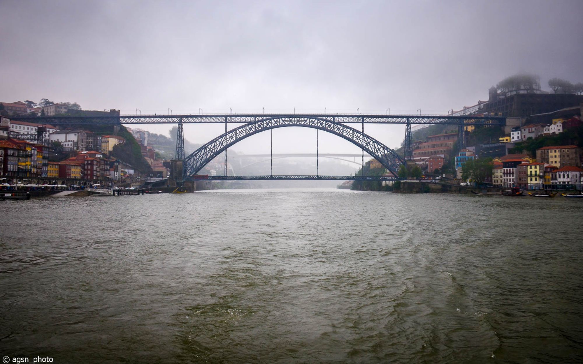 Blick von einem Schiff auf eine große Stahlbrücke, die zwei Städte verbindet, aufgenommen bei schlechtem Wetter.