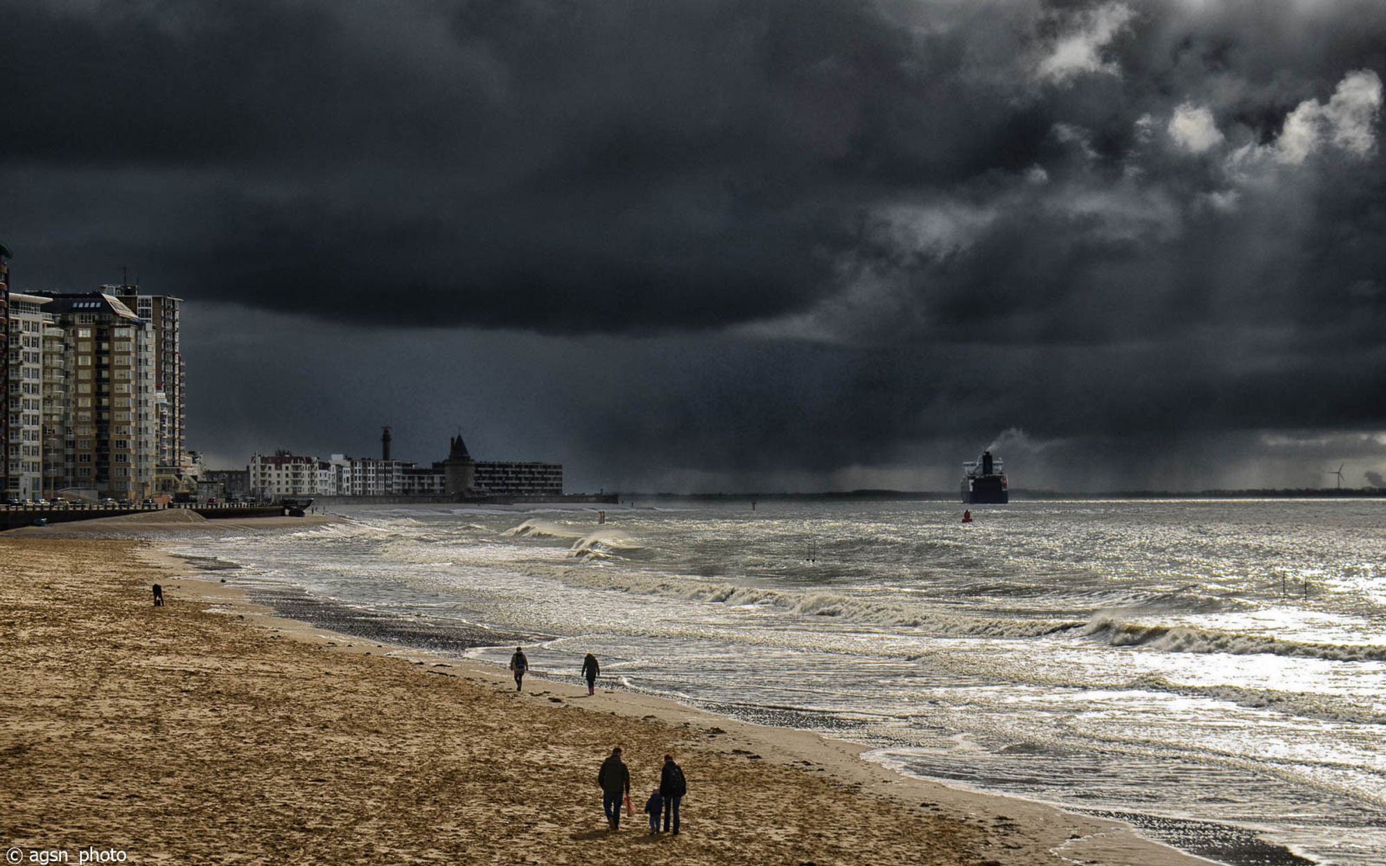 Dunkle Regenwolken über der Westerschelde bei Vlissingen/NL. Links die Hochhäuser am Boulevard, einige Menschen am Strand, auf dem Wasser ein Frachtschiff auf dem Weg zum Hafen von Antwerpen.