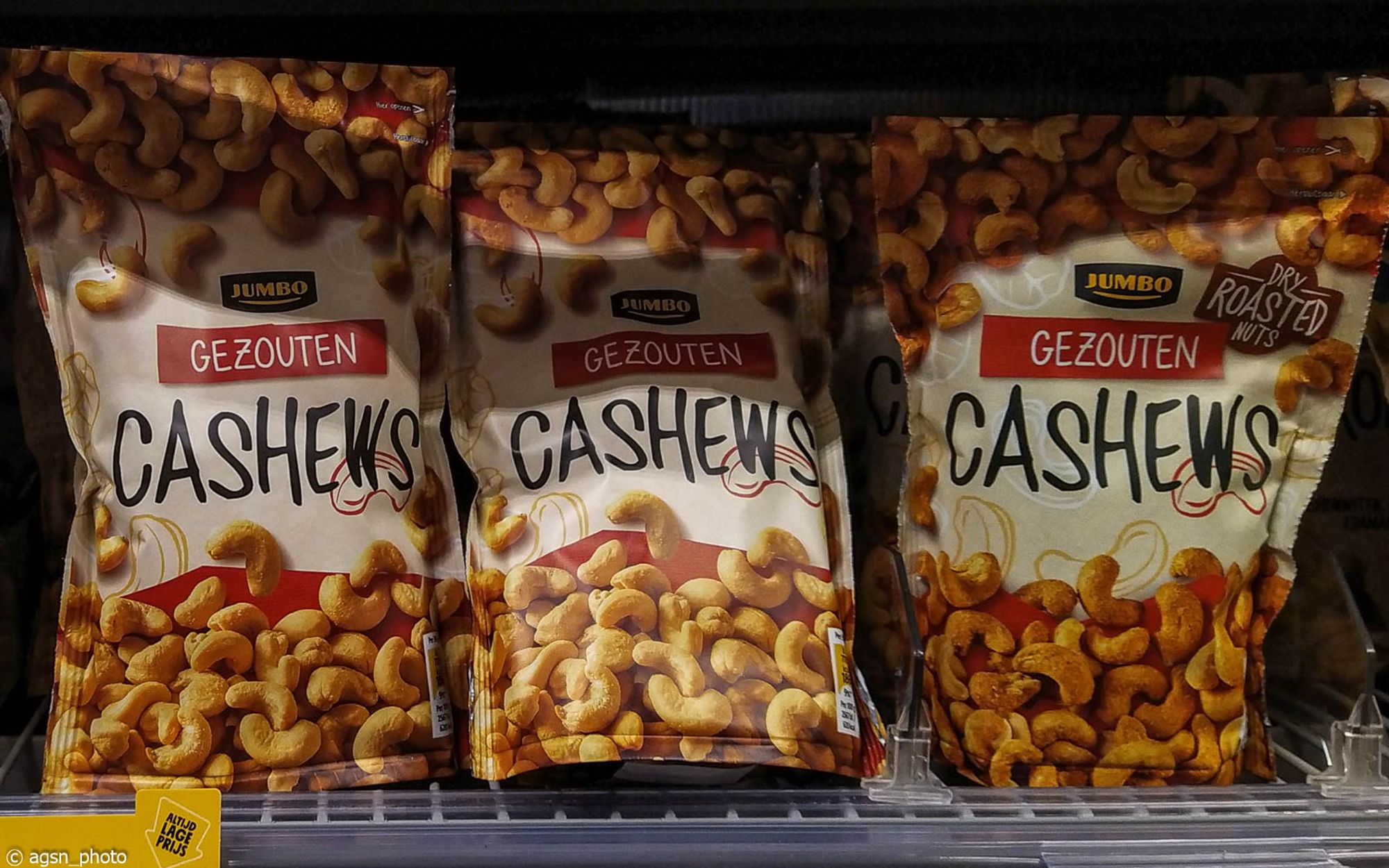 Drei Packungen gesalzene Cashewnüsse stehen aufgereiht im Regal eines niederländischen Supermarktes.