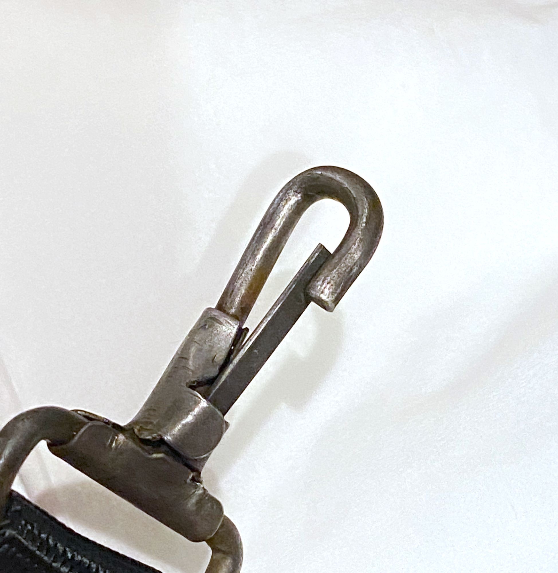 a metal spring clip against a white background. It's scratched and pitted but grey, not rusty, and clearly solid and functional.