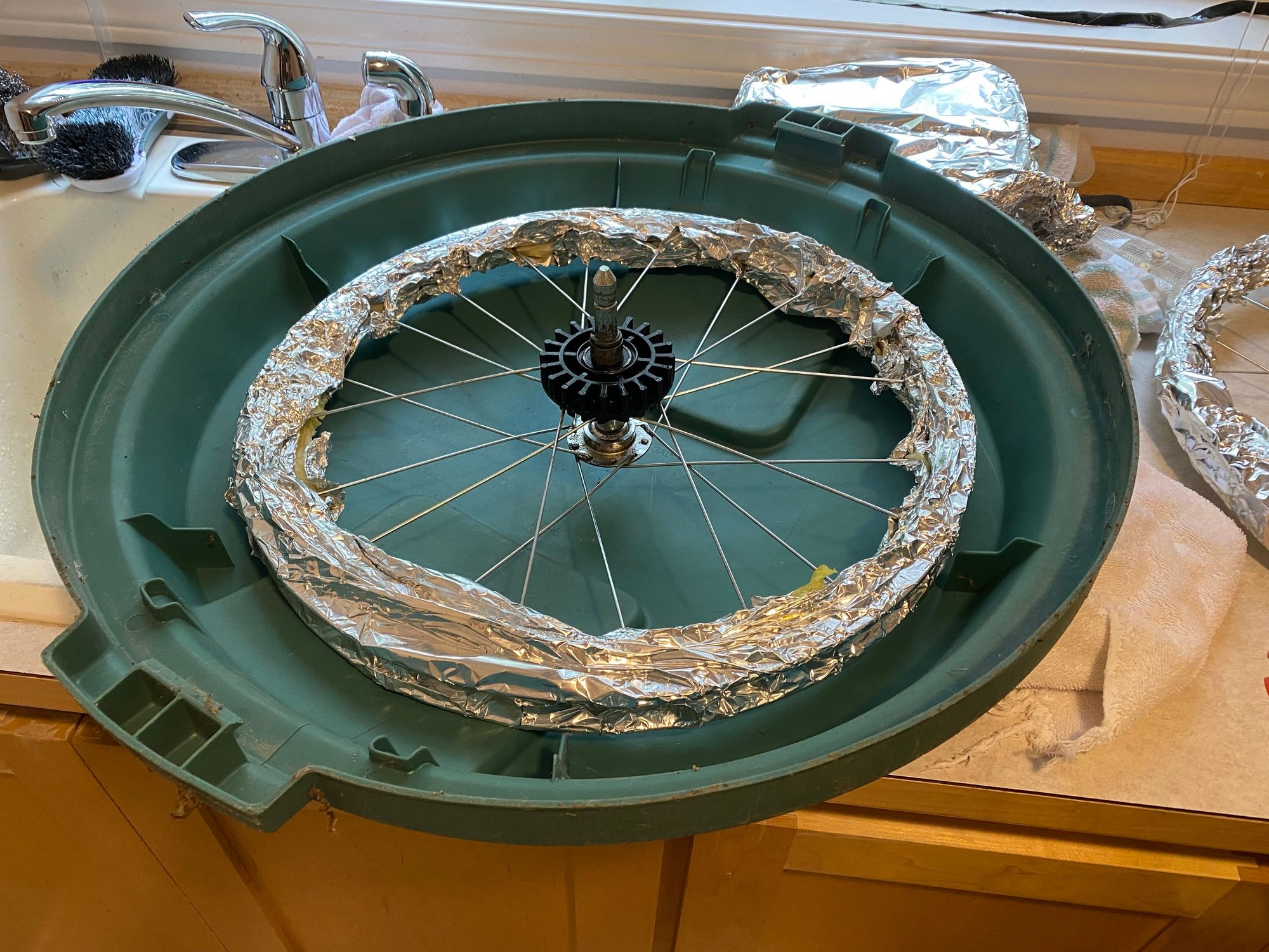 an upside-down 32-gallon garbage can lid made from green plastic with the bike wheel sitting in it