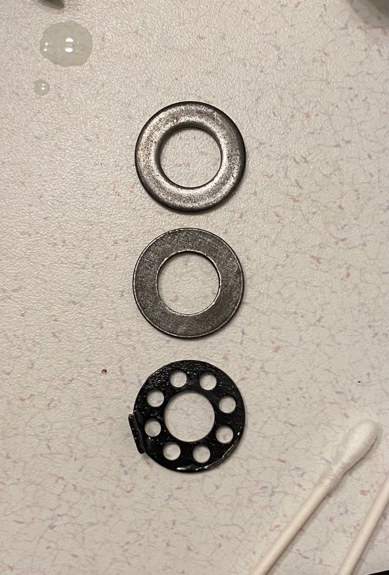 two silverish washers and a reference black circle on a countertop. the upper plated washer looks shinier but that’s mostly texture of top side of a stamped style washer