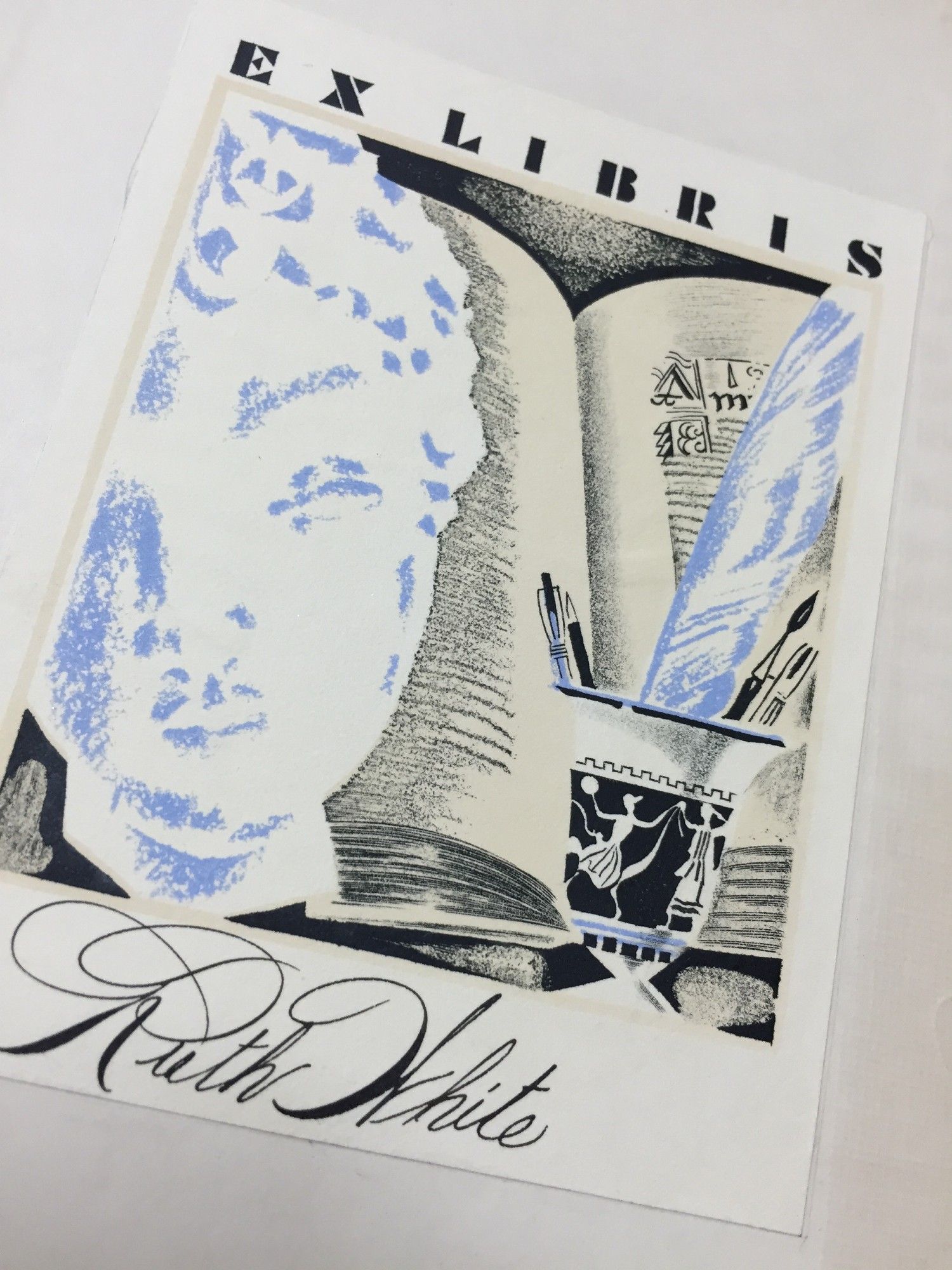 Bookplate with a woman's face and cup holding pens and brushes with an open book in the background.