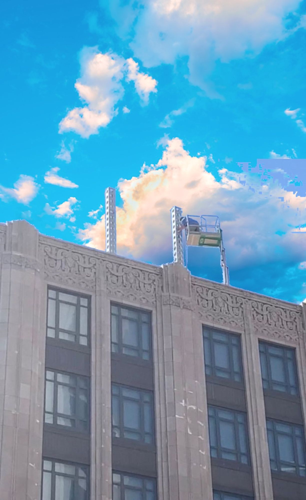 The former Twitter headquarters with the scaffolding remaining from where the giant metal X has been taken down superimposed over the cloudy blue sky seen in the logo for the BlueSky app, the image that fills the phone screen while the BlueSky app is loading.