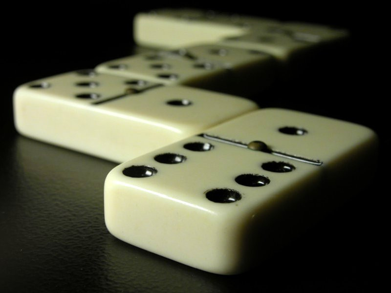 A picture of dominoes. They are lying resolutely on a leather surface, tastefully lit from the side at a very low angle