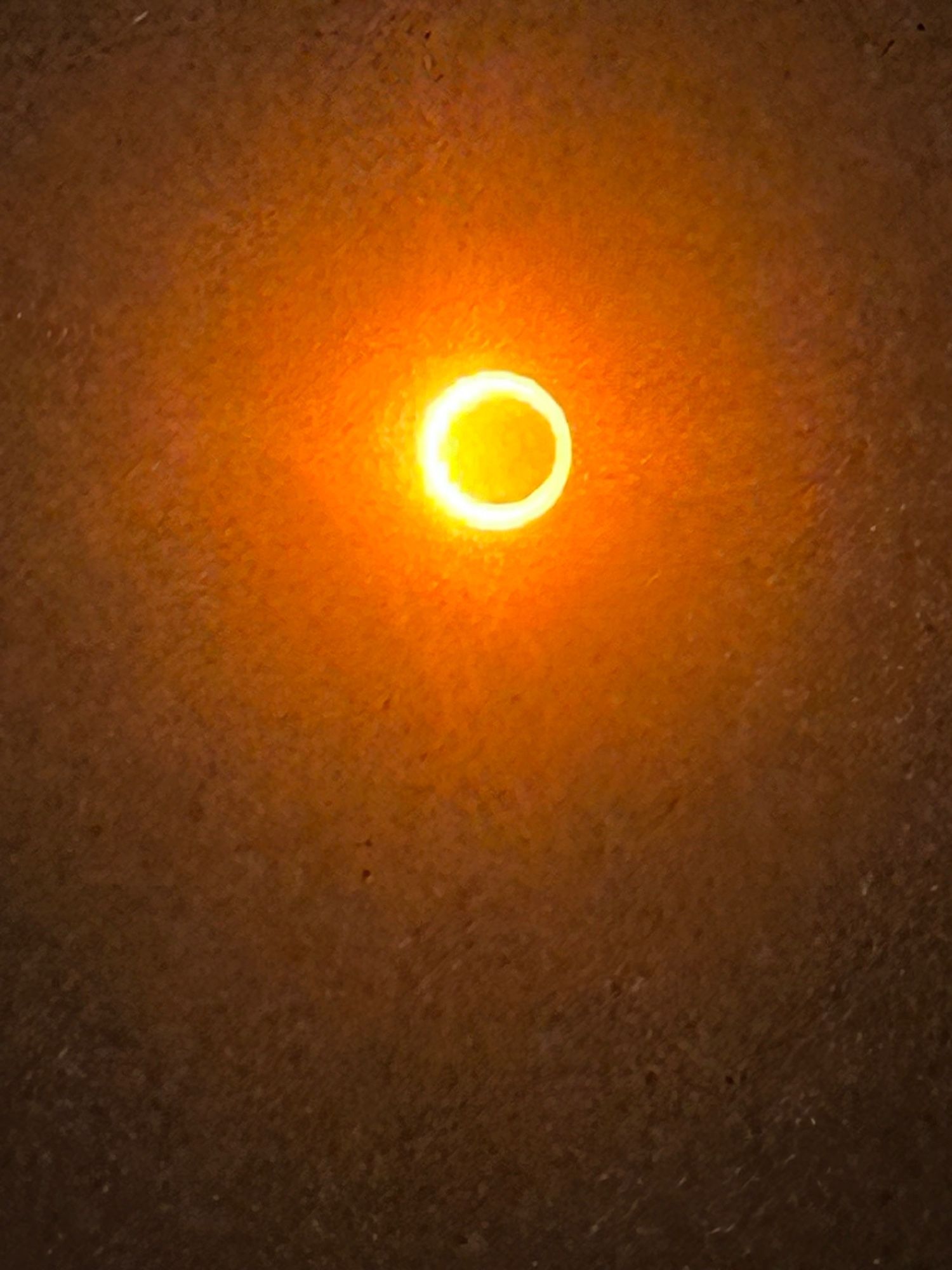 A photograph of an annular solar eclipse, the sky is darkened and the sun has the dark circle of the moon in front of it, surrounded by a ring of fire