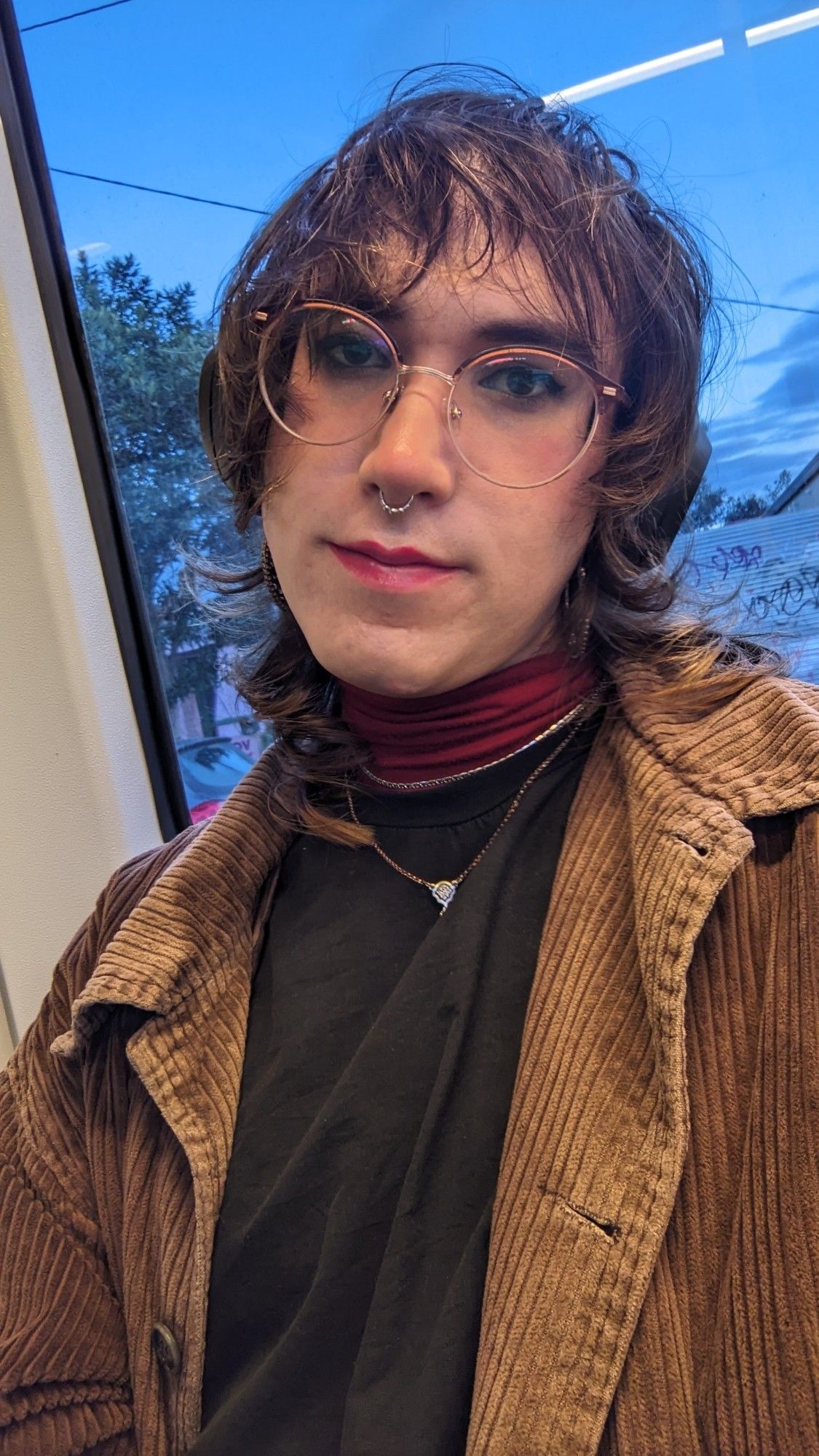 Woman on a tram wearing an orange turtleneck under a black dress, with a brown jacket.