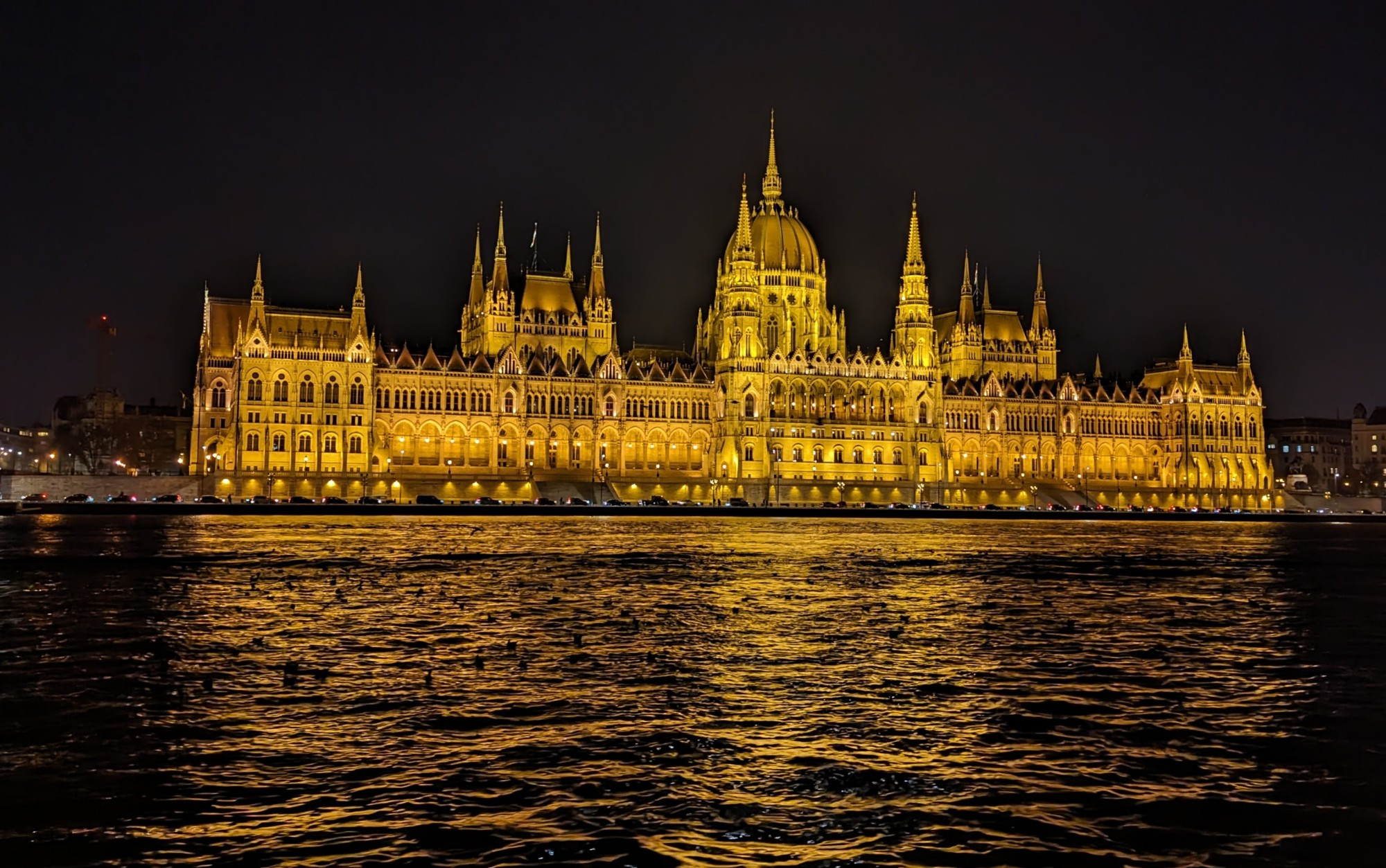 The photo shows the Hungarian Parliament Building illuminated at night. It is reflected in the water of the Danube River.
