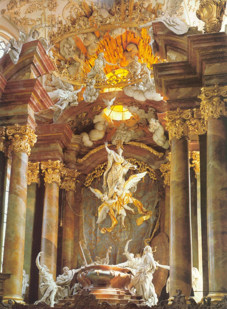 A theatrical stucco altarpiece of the Assumption of the Virgin, featuring life-size statues of the disciples gathered round a tomb and looking up in astonishment as the Virgin Mart is lifted toward a tinted skylight with stucco angels, clouds, and beams of light