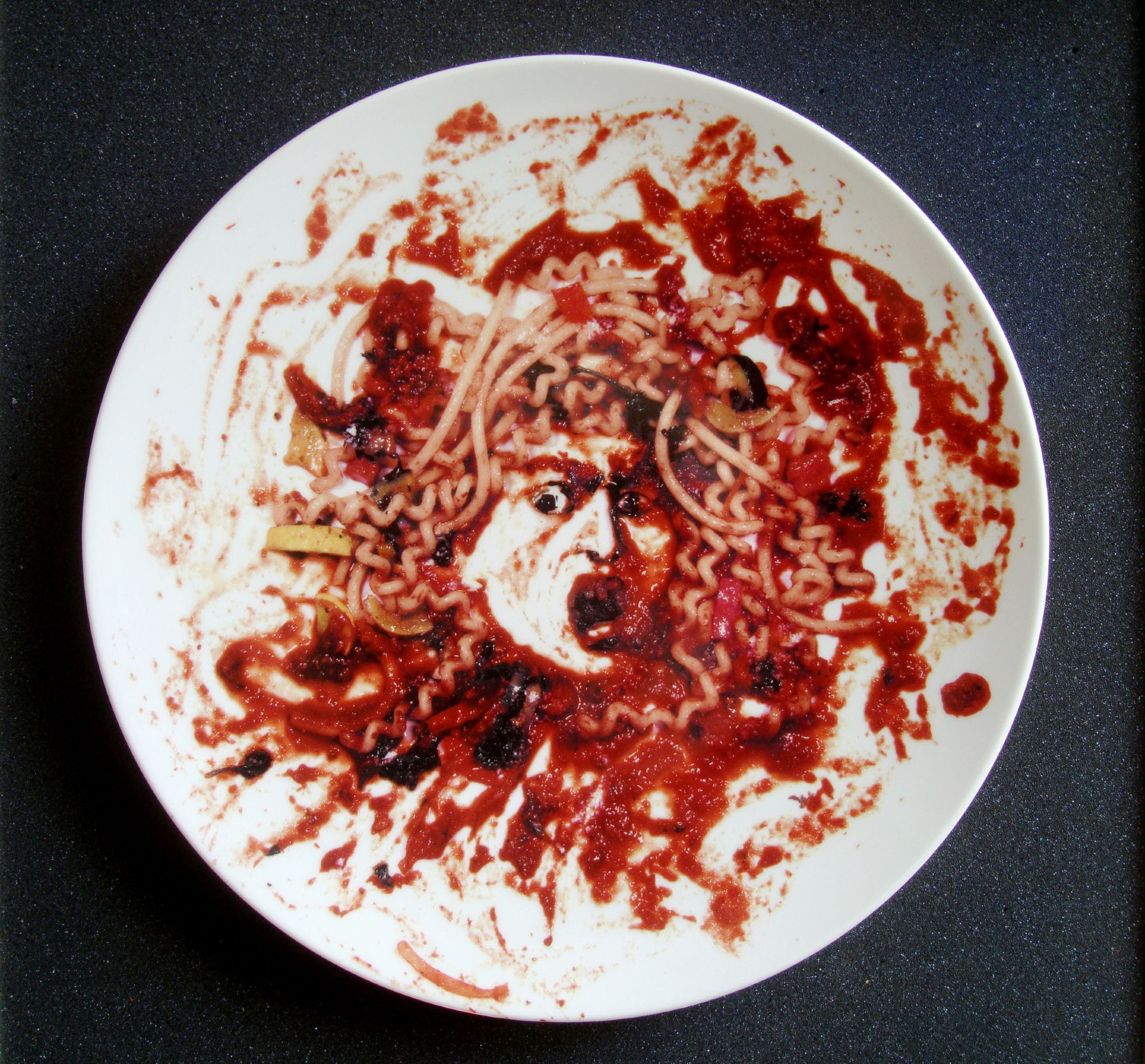 A photograph of a screaming gorgon's head made of pasta and marinara sauce printed on a porcelain plate.