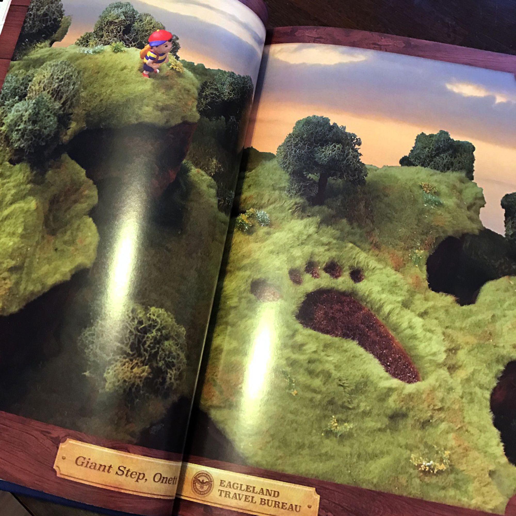 Fangamer's EarthBound Handbook open to the two page spread of Meeellla (aka Camille Young)'s large scale model of Ness overlooking Giant's Step.