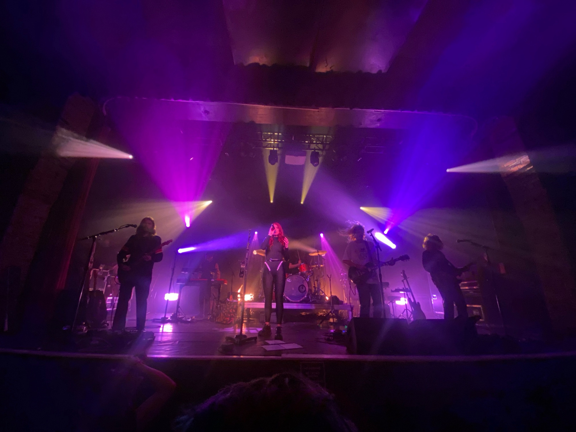 four members of the band grouplove are backlit with purple stage lights, performing a song.