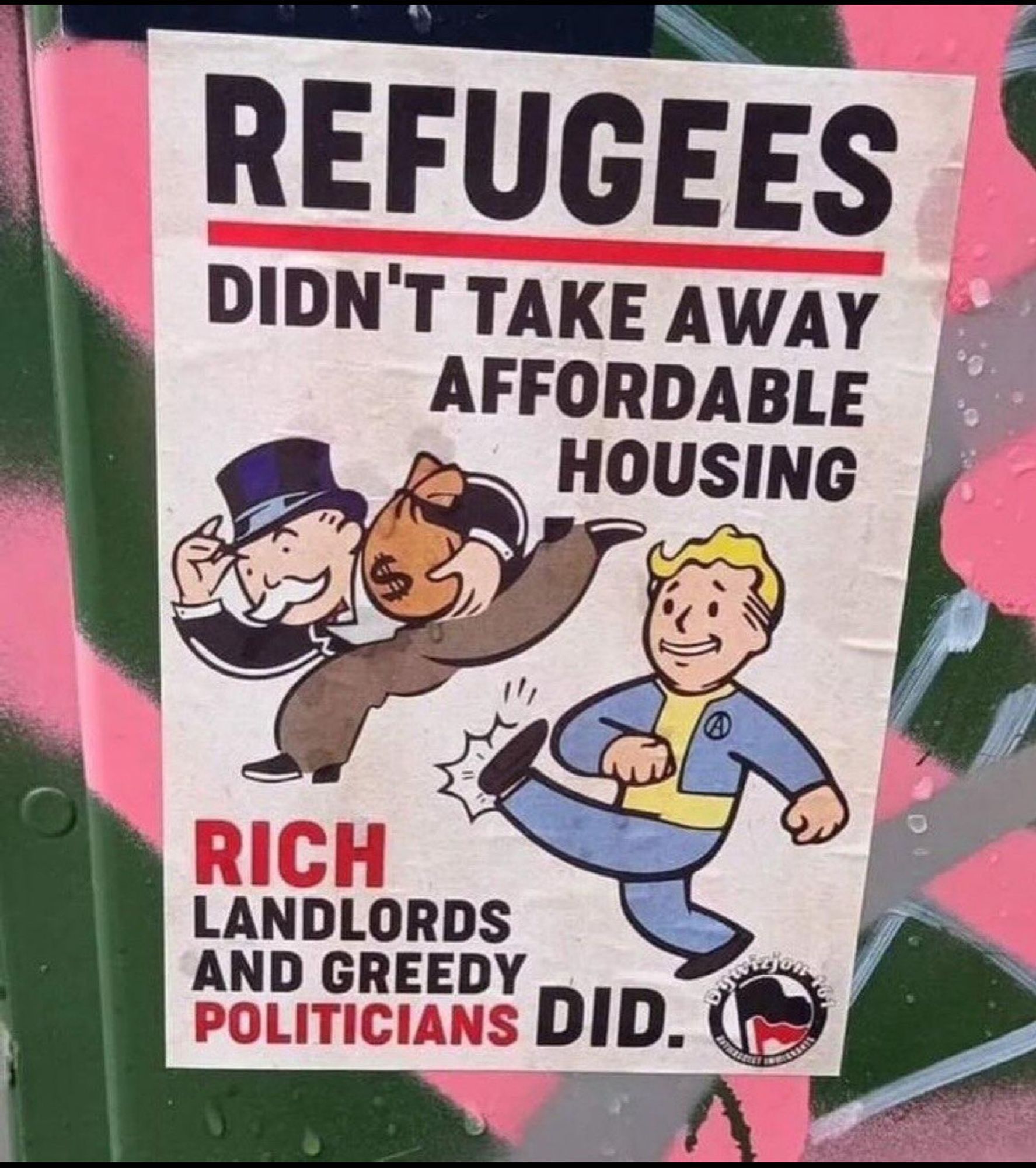 auf einem Poster, das an eine grün/rosa verspayten Wand gekleister wurde, sind der fallout-pip-boy der dem monopoly-männchen in den arsch tritt, sowie das antifa-logo zu sehen. Dazu der Text: 

REFUGEES ( Rot unterstrichen ) 
DIDN'T TAKE AWAY AFFORDABLE
HOUSING

RICH ( rot unterstrichen ) LANDLORDS AND GREEDY  POLITICIANS ( rot unterstrichen )  DID.


