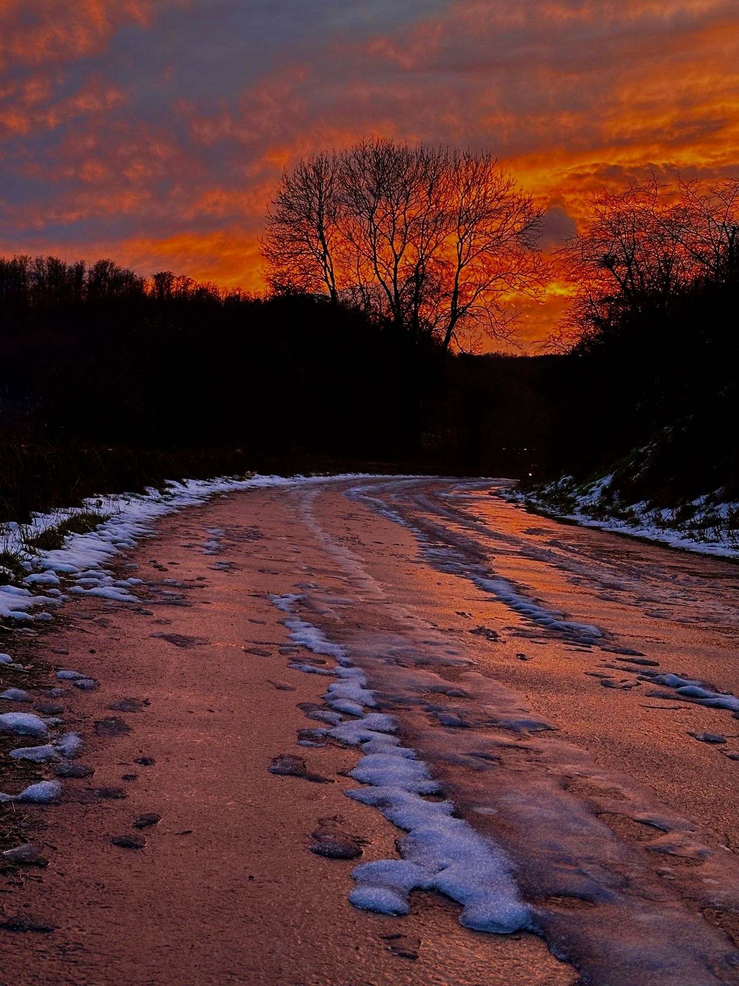 Sonnenaufgang mit einer vereisten Straße auf deren Asphalt sich die Sonne rötlich spiegelt