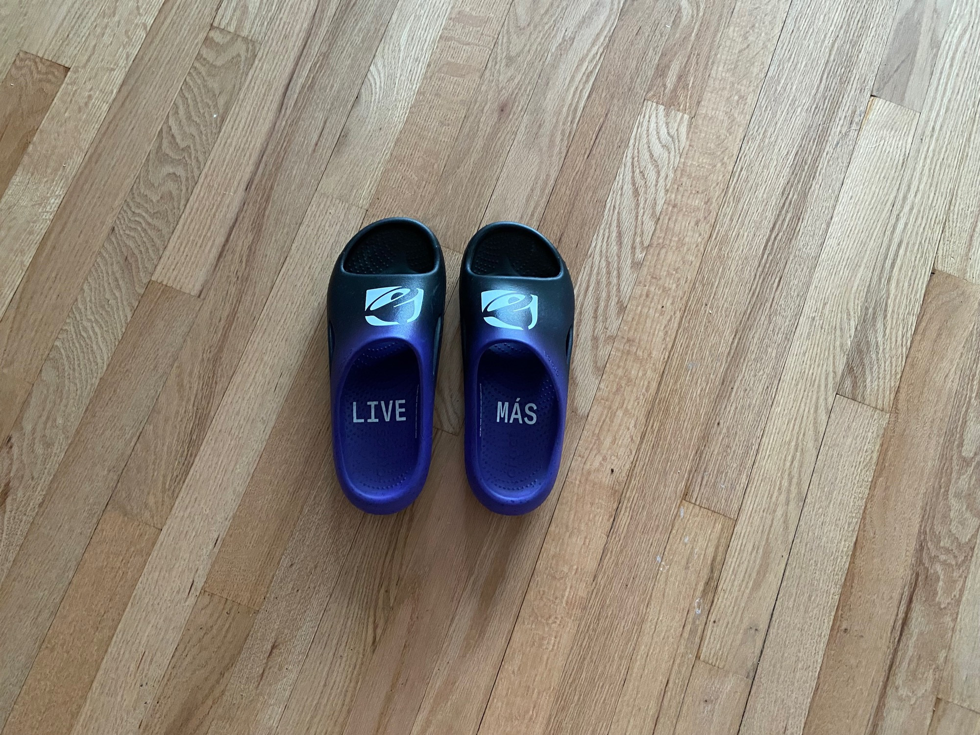 purple and black croc slides with the taco bell logo on the top and the words “live más” on the inner soles