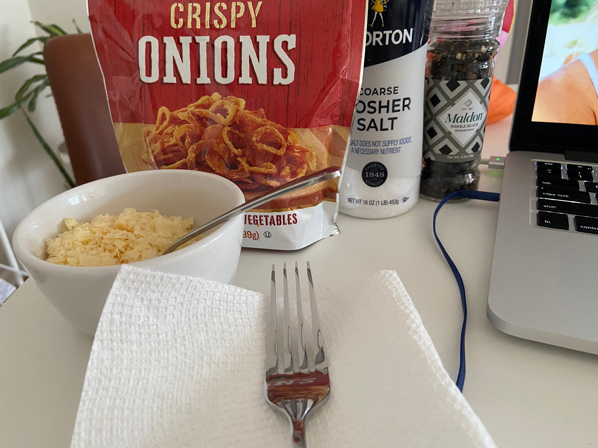 fork on a paper towel, bowl of shredded cheese, bag of crispy onions, kosher salt, plastic pepper grinder, laptop