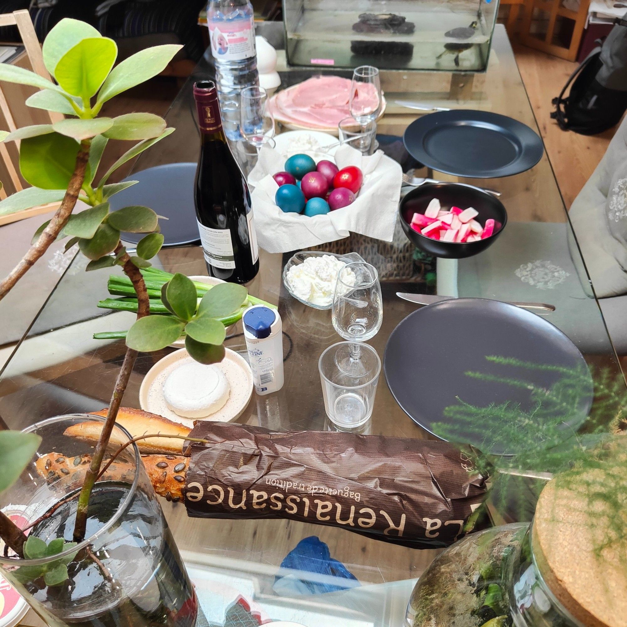 Une table avec des œufs colorés, des radis, du fromage blanc et du jambon