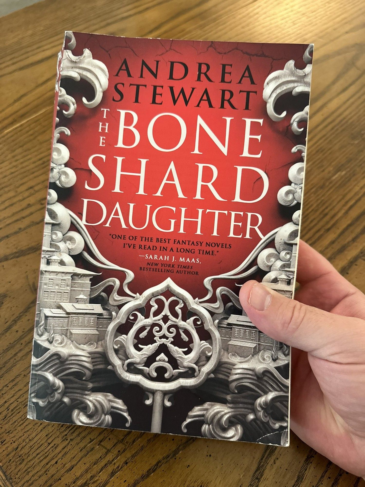 Book cover of THE BONE SHARD DAUGHTER, by Andrea Stewart. A central crimson background is framed by intricately-carved bone sculpture depicting cities and ocean.