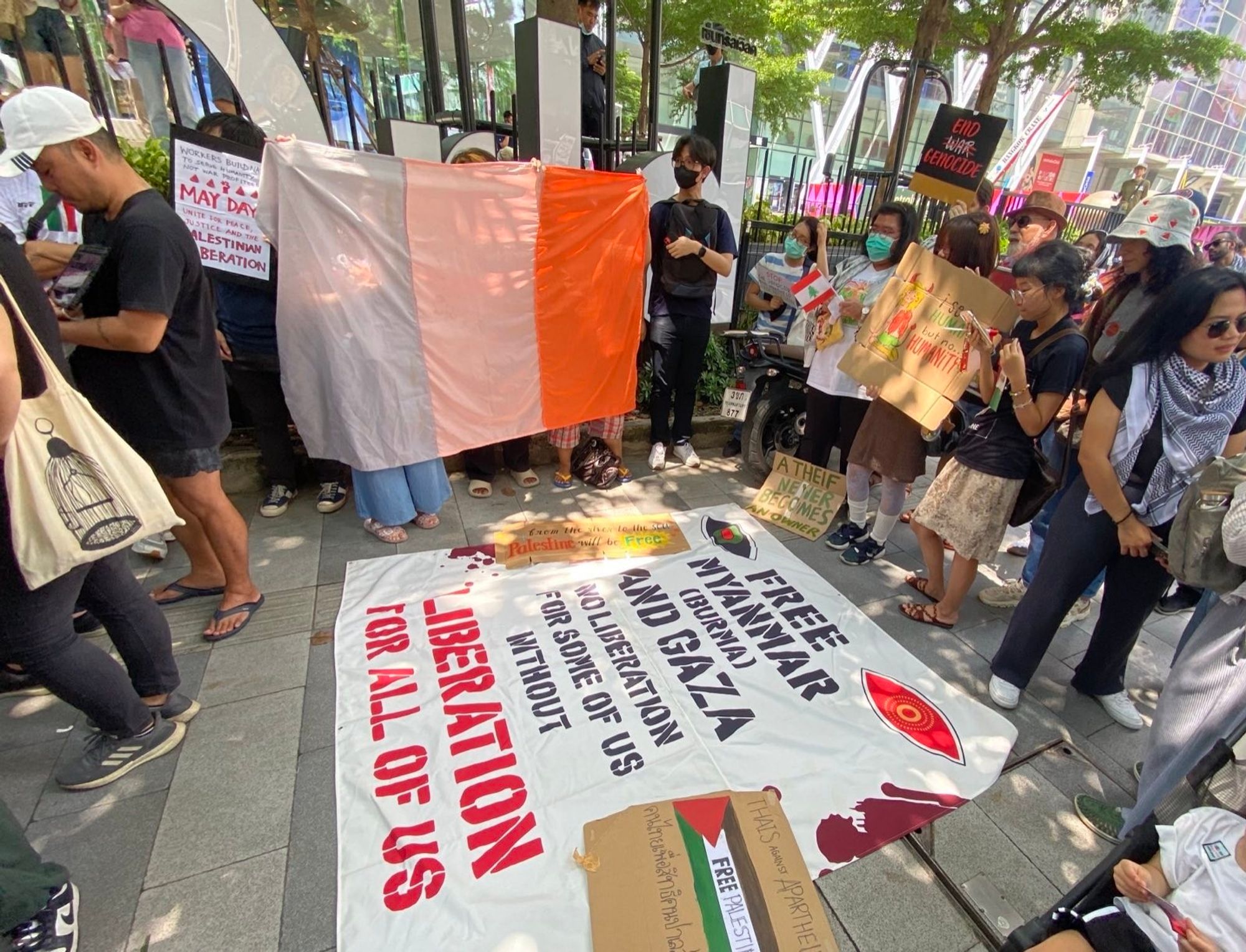 Activists holding up the "flag" of the MilkTeaAlliance along side a big banner that reads free Myanmar (burma) and Gaza, no liberation for some of us without liberation for all of us.