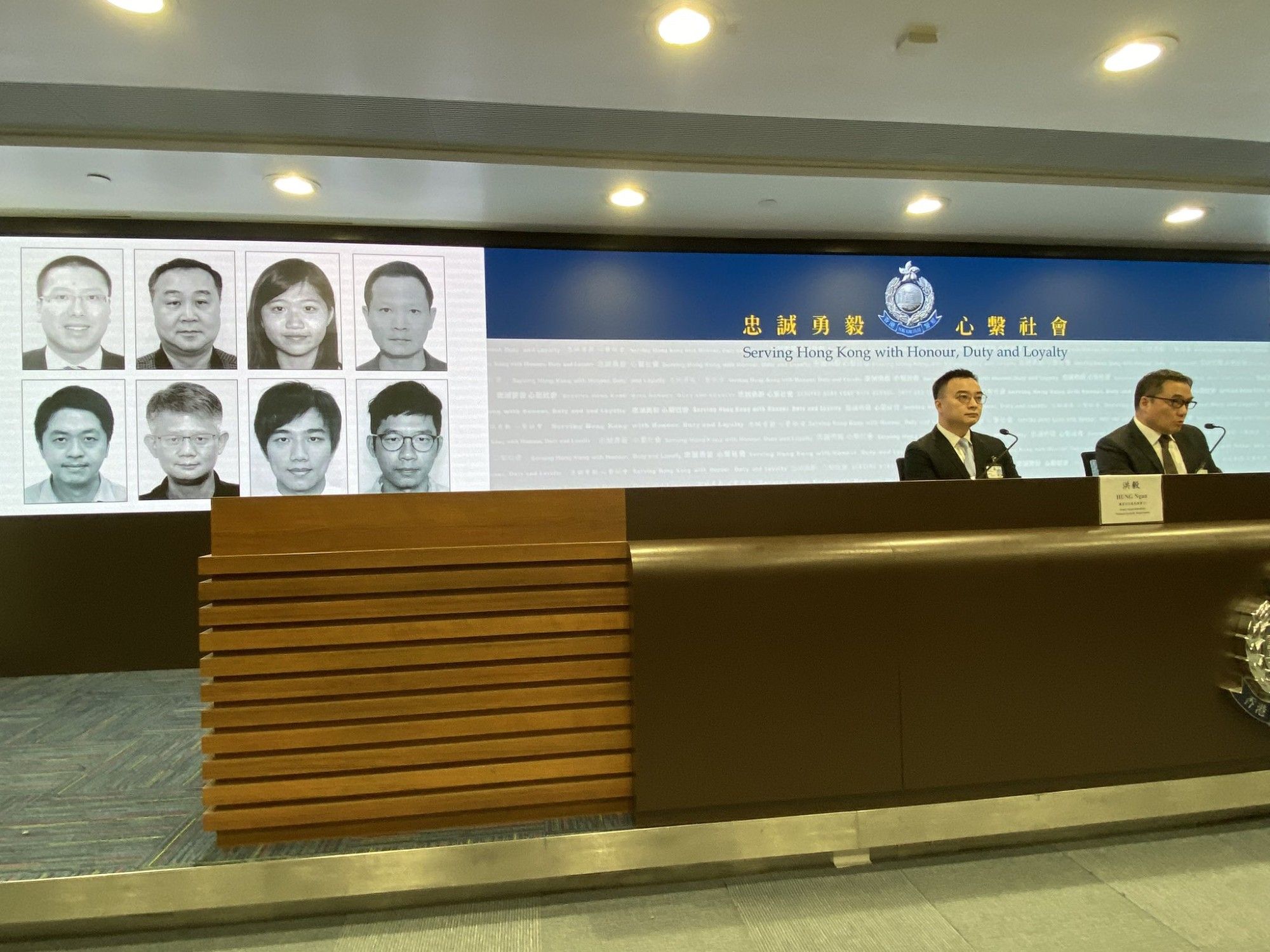 Picture of two National security law police announcing new arrest warrants with pictures of the 8 people they have issued warrants for. 