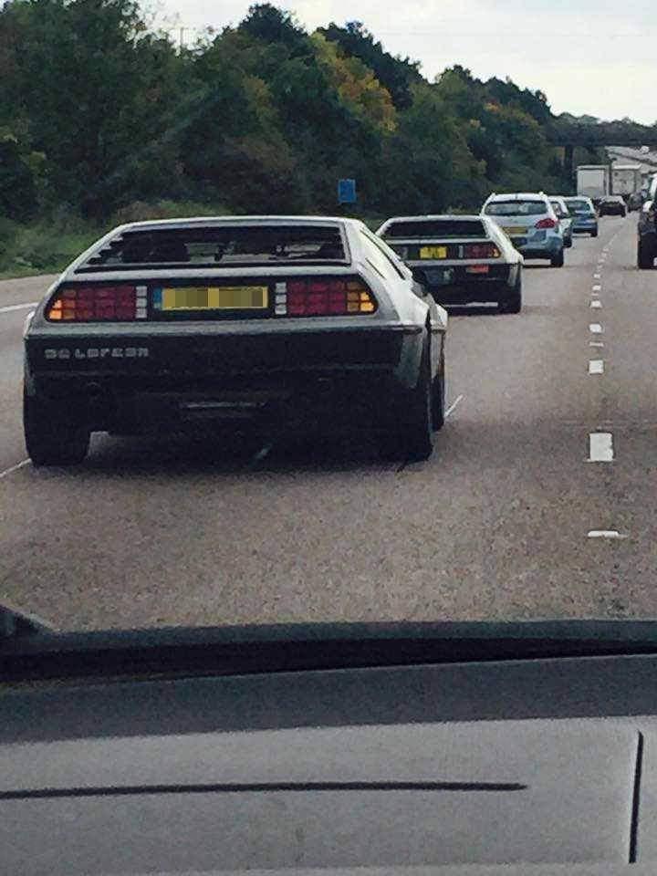 Two Delorean cars, one behind the other, on a busy motorway 