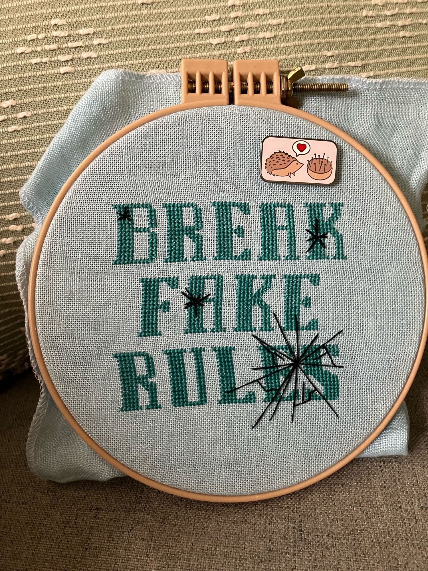 Cross stitch piece of blocky text “break fake rules” with glass cracks running through