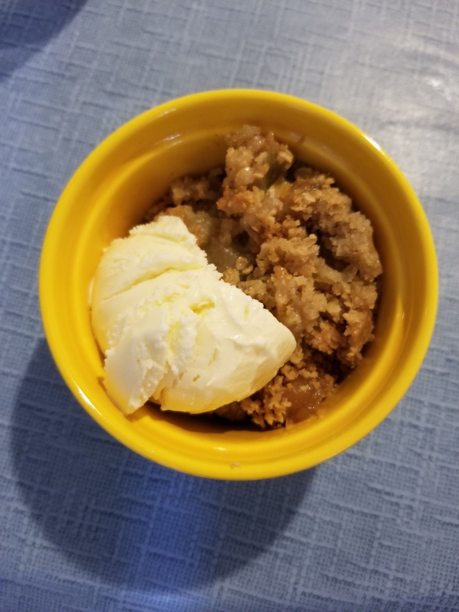 Rhubarb and pear crumble with vanilla ice cream in a yellow ramekin