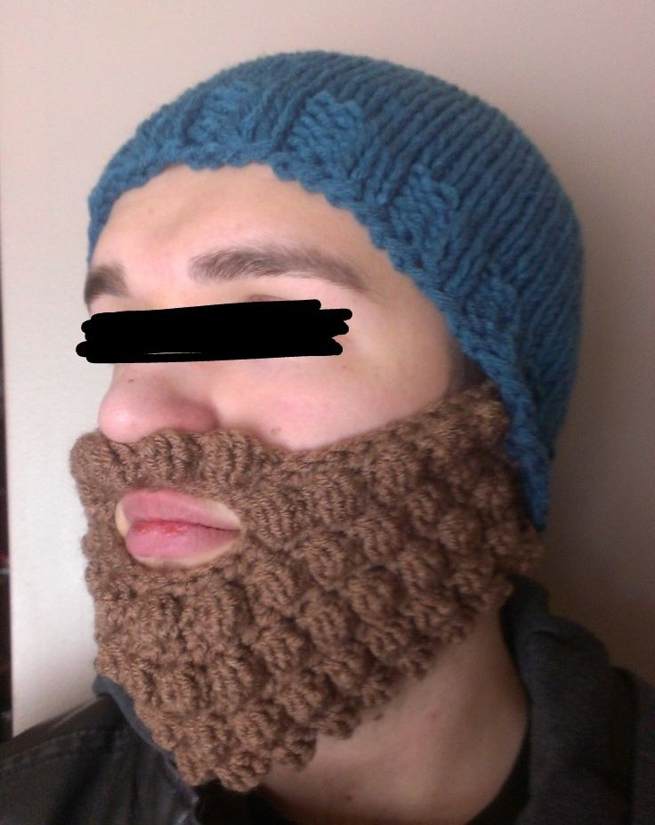 Face of a person wearing a blue knit beanie with a brown crochet beard & mustache