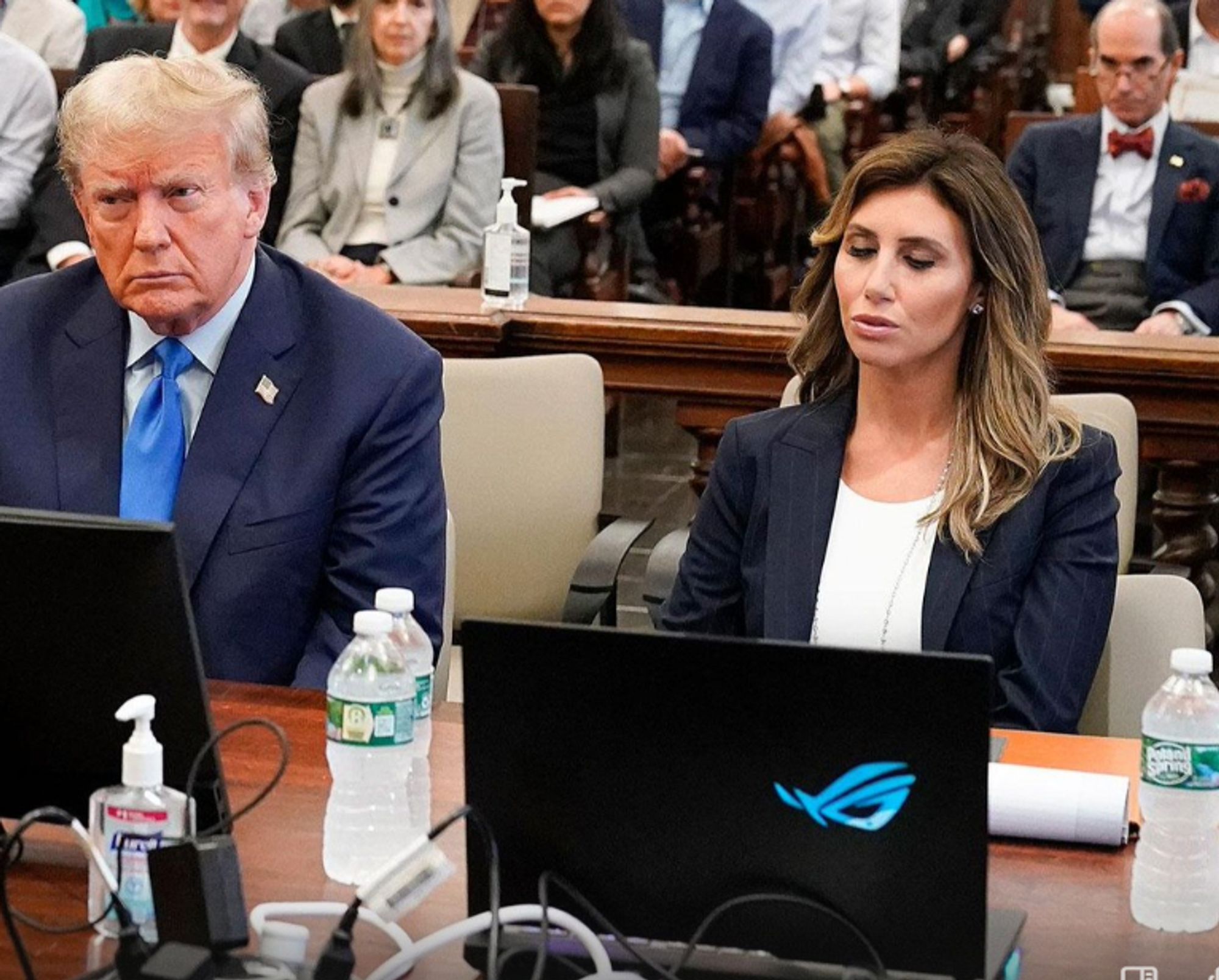 Donald Trump (L) and one of his lawyers, Alina Habba. Habba is using an Asus "Republic of Gamers" gaming laptop. The LED lights on the emblem are glowing blue. In a post upthread they are glowing red-orange, indicating that the lights are cycling through colors in the courtroom.