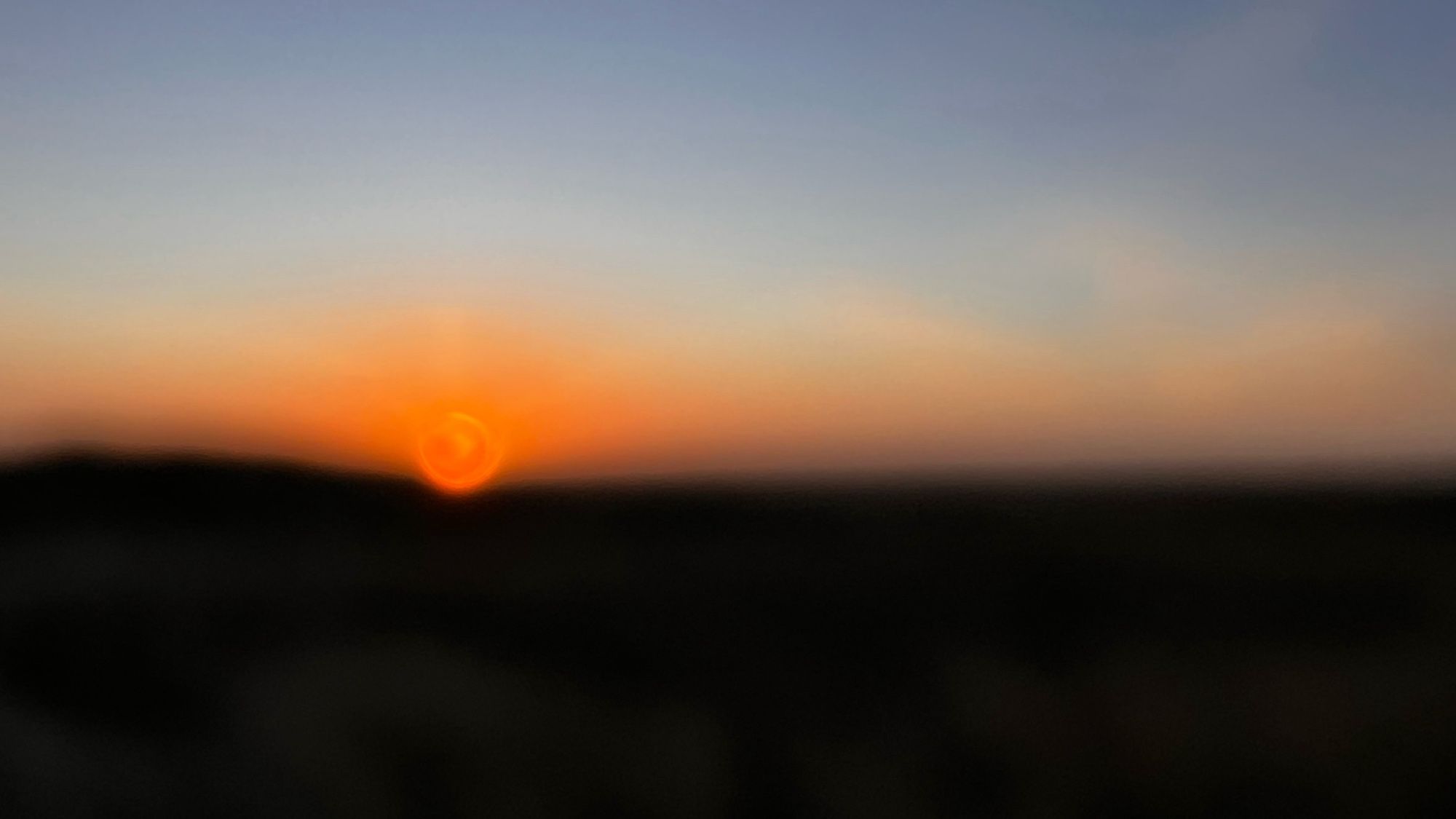 Zonsopkomst waarbij de zon als een gloeiende magma bal net boven de horizon uitkomt. Het beeld is niet scherp en loopt van beneden naar boven van zwart naar gloeiend rood naar blauw.