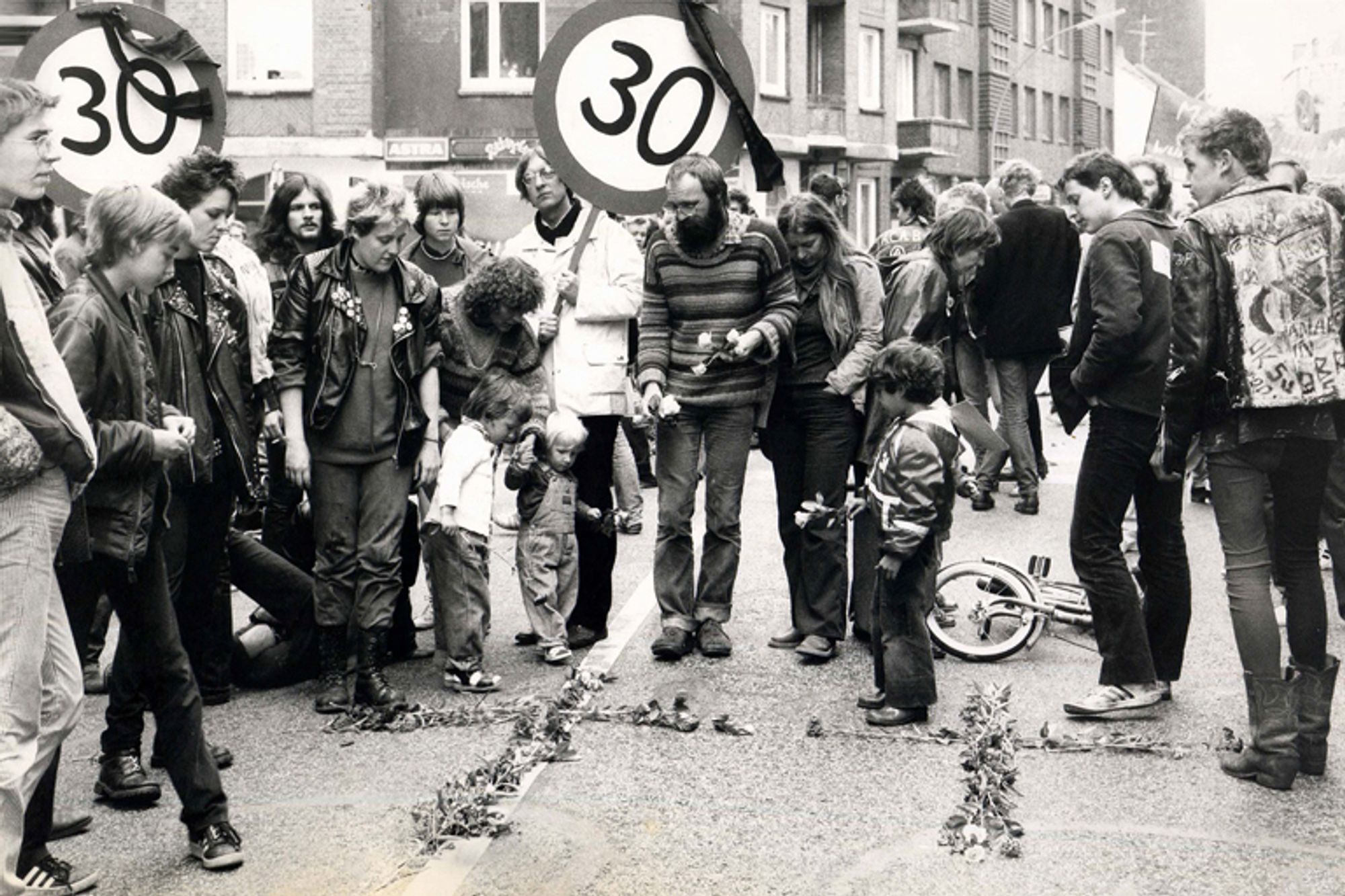 Schwarz-Weiß-Foto
Demonstranten mit Tempo-30-Schildern, auf der Straße zwei Kreuze aus Blumen