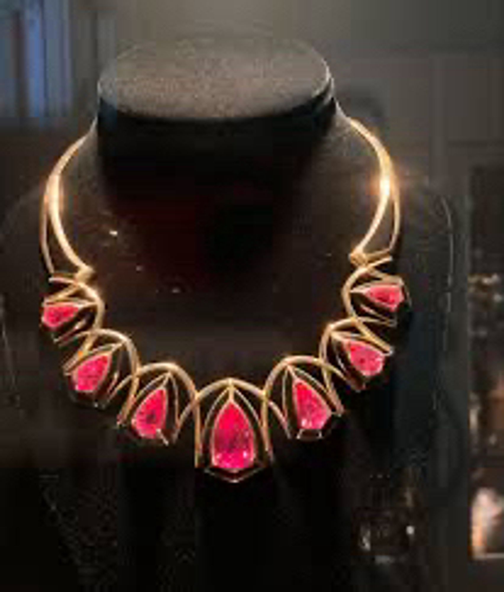 A gold necklace set with seven bright pink gems displayed on a black plastic mannequin bust