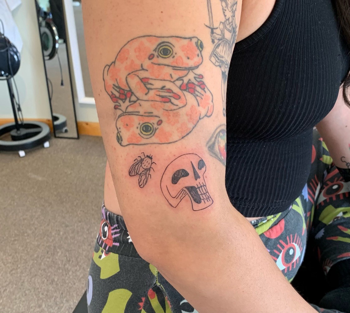 Upper arm with some cool tattoos of frogs a fly and a skull